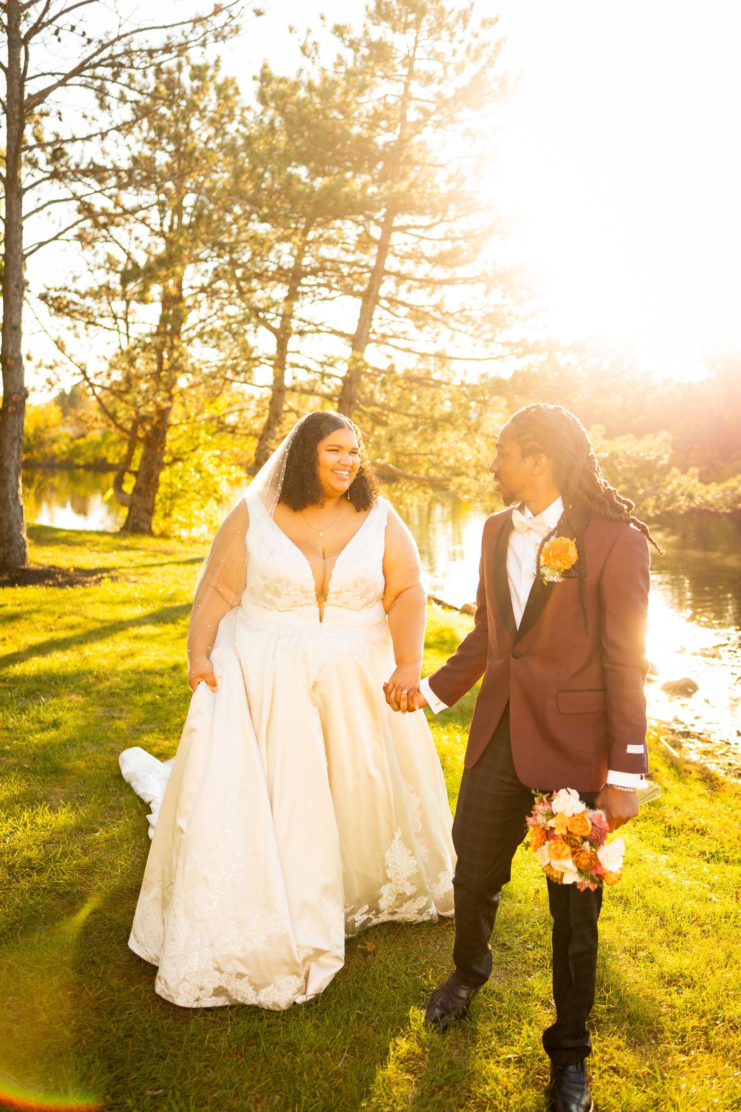 A couple walks hand in hand through a sun-drenched meadow during golden hour at their outdoor wedding celebration.