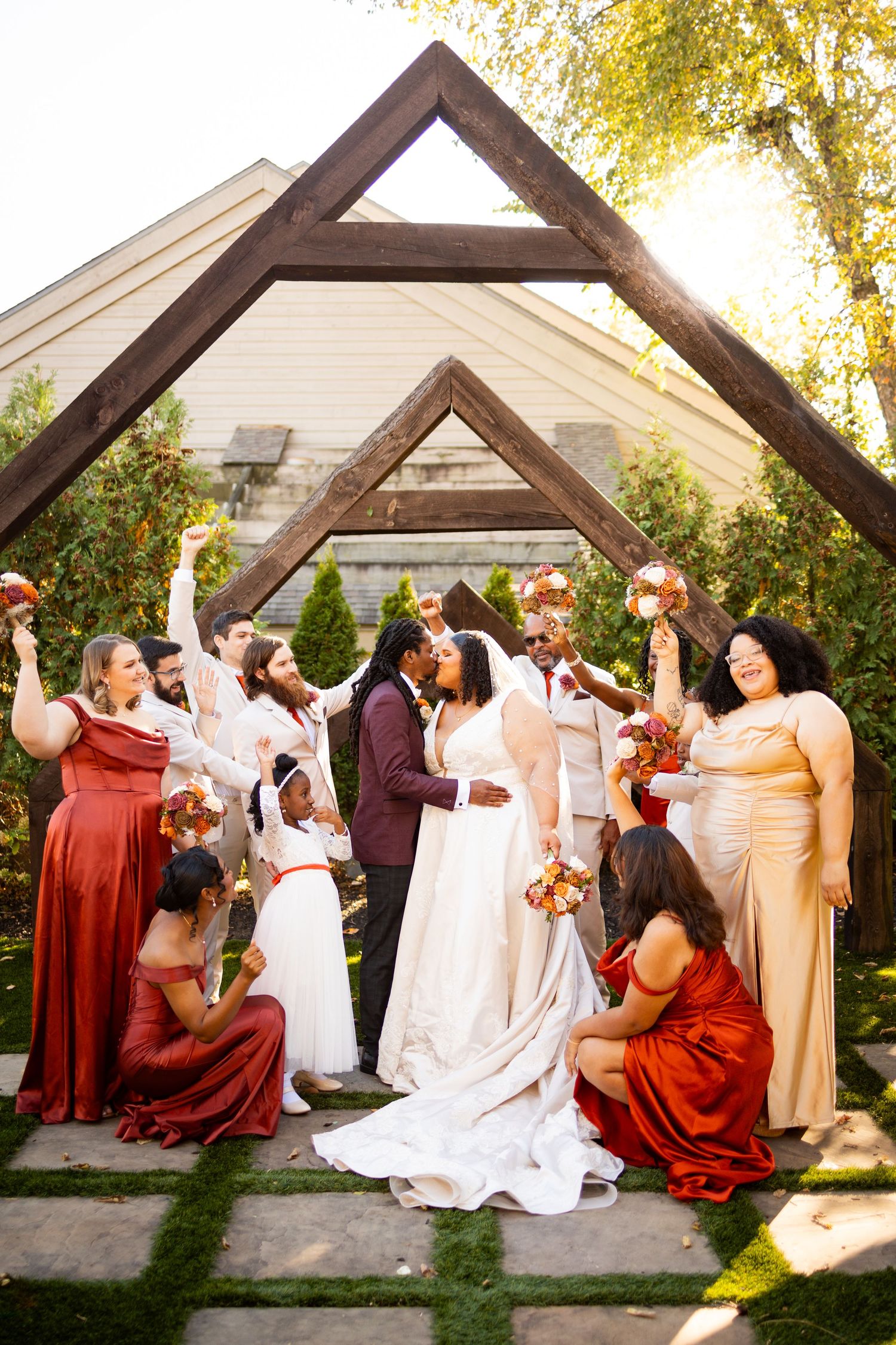 A wedding party performs a choreographed dance routine under a wooden arch during an outdoor celebration.