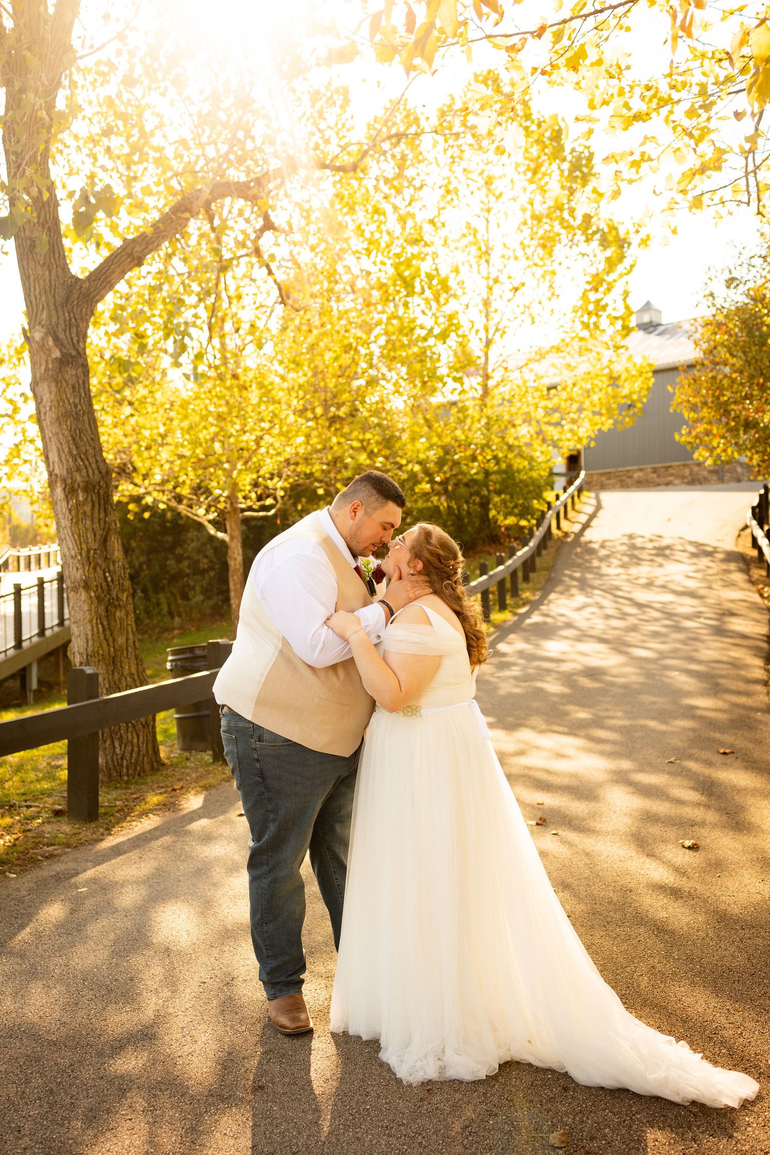 Romantic couple shares tender moments in golden autumn sunlight along tree-lined path during outdoor wedding photoshoot.