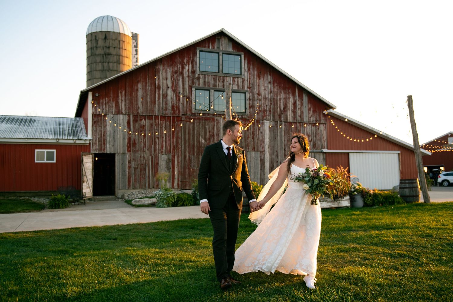 A rustic wedding celebration at a charming red barn venue with scenic farmland views at sunset.