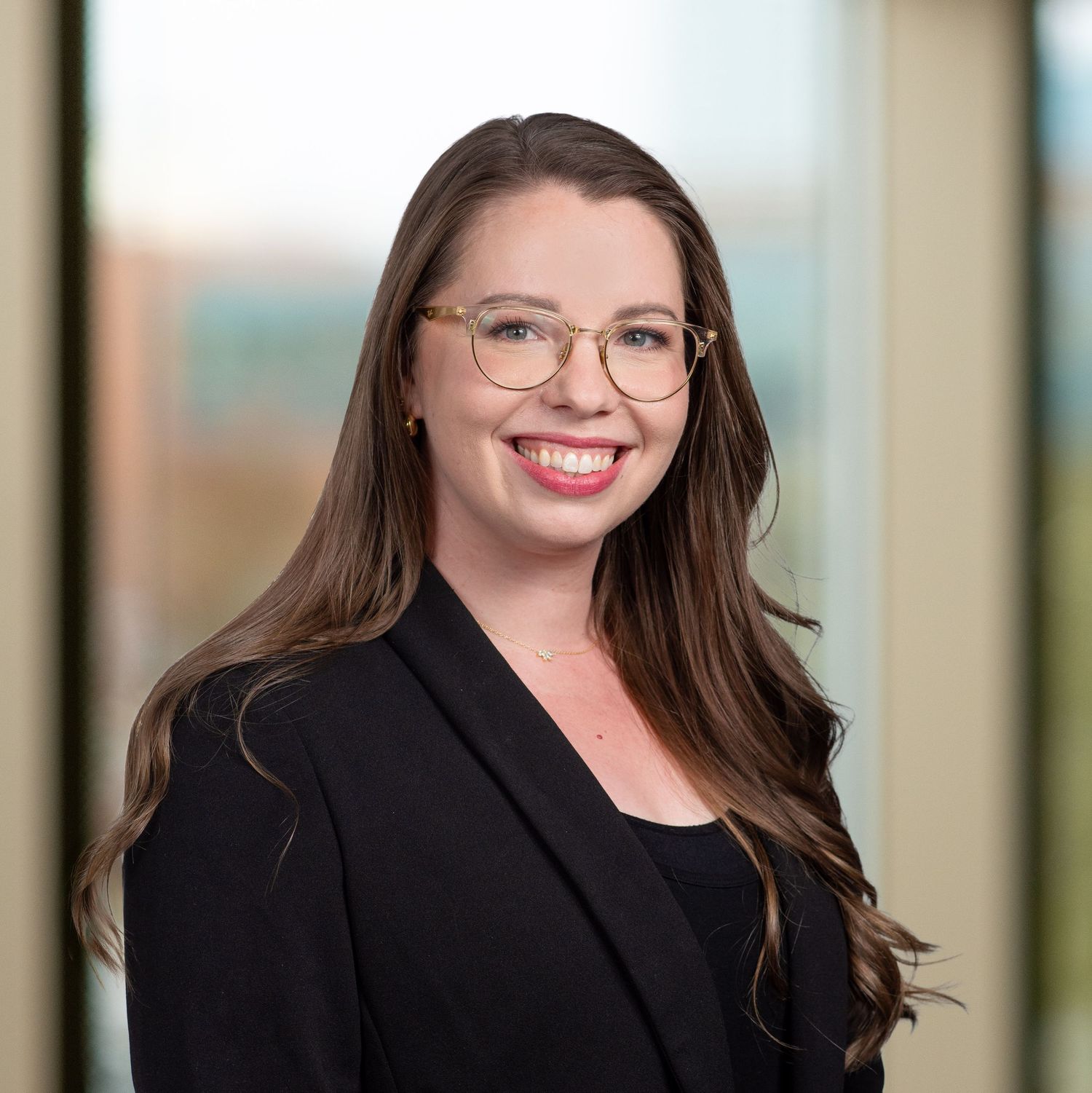 Professional headshot of a financial advisor in a black blazer and glasses smiling warmly against a blurred office background.