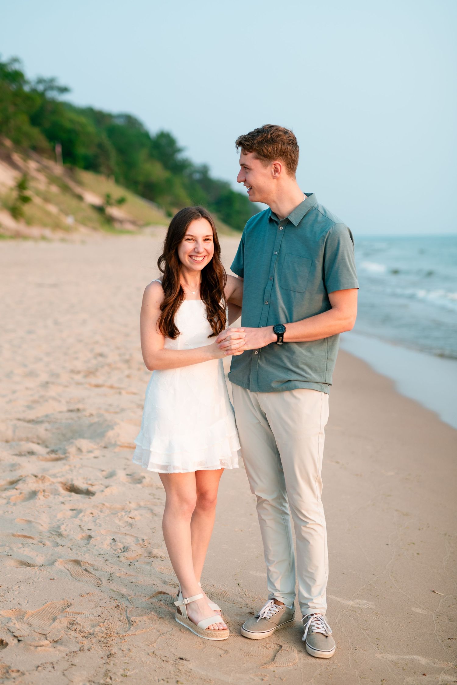 Couple walking together on a sandy beach sharing intimate moments in casual summer attire near the ocean.