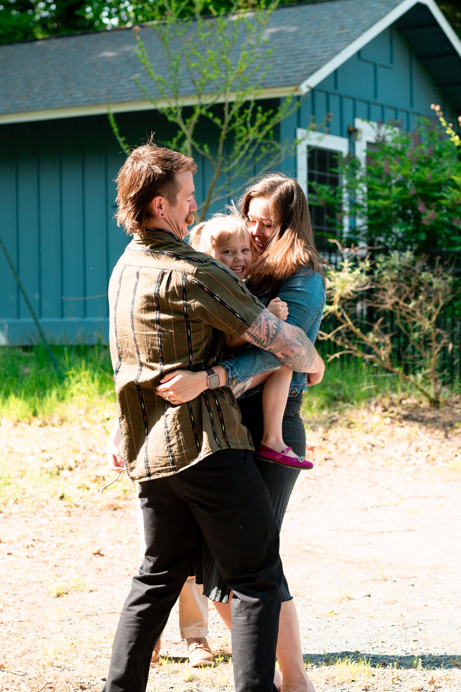 A couple embraces and laughs together outside a blue house on a sunny day.