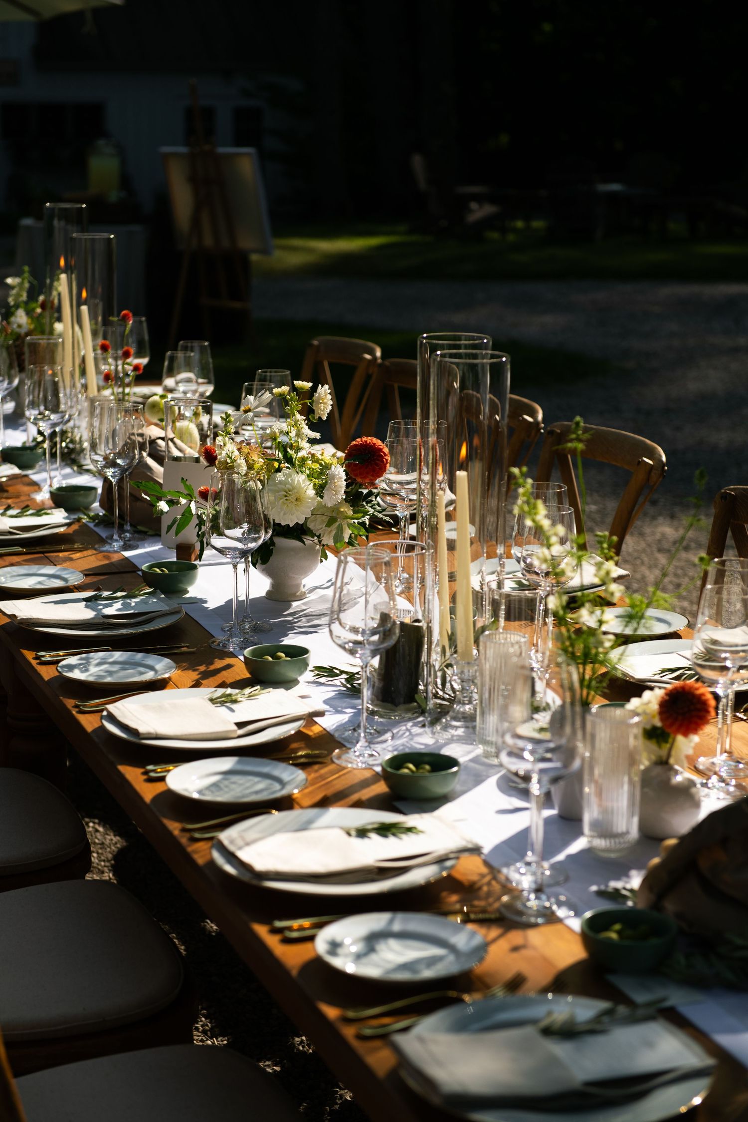 Elegant table settings with white plates, wine glasses, and floral centerpieces arranged on a rustic wooden table.