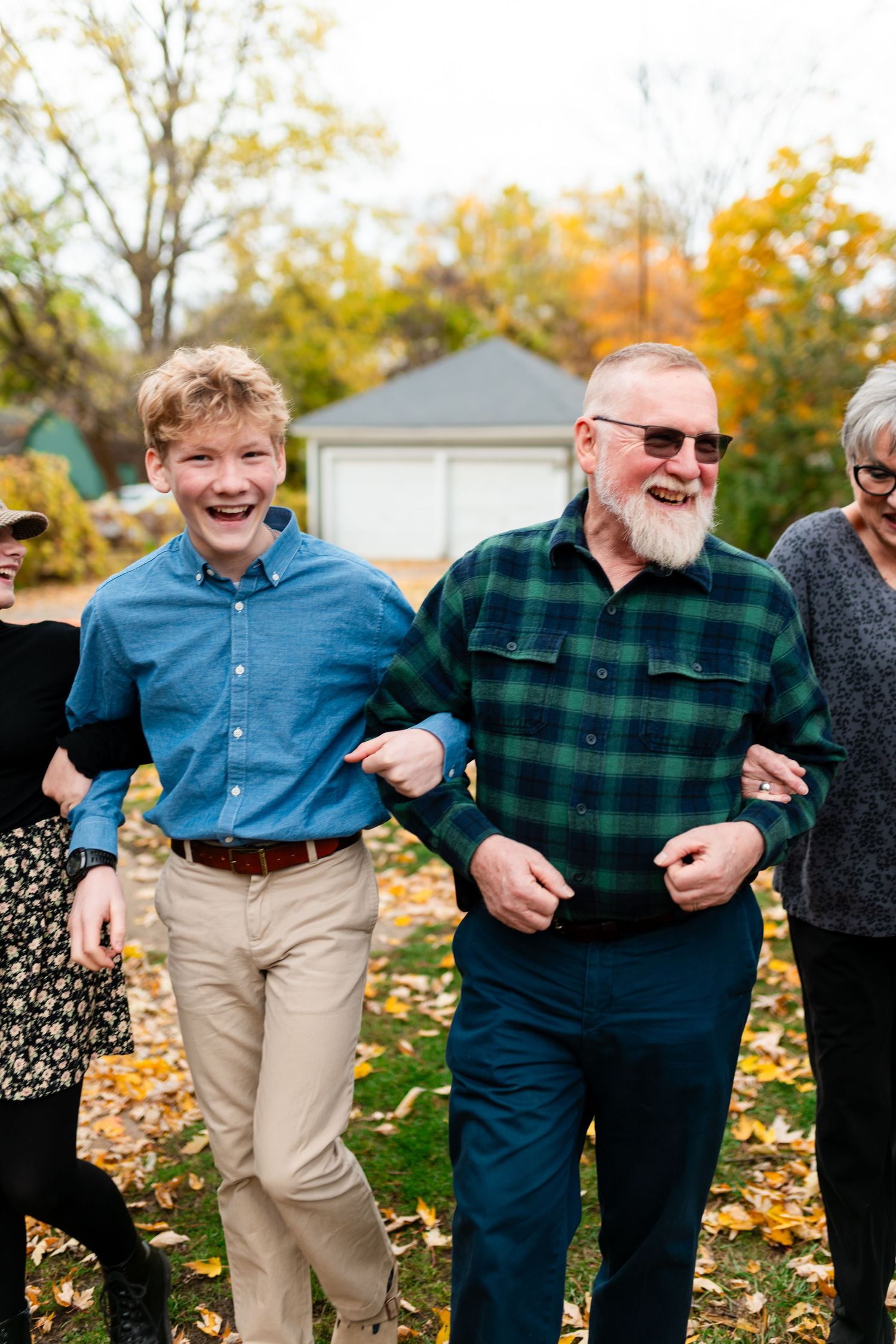 A group of people walking together and laughing outdoors on an autumn day with fallen leaves on the ground.