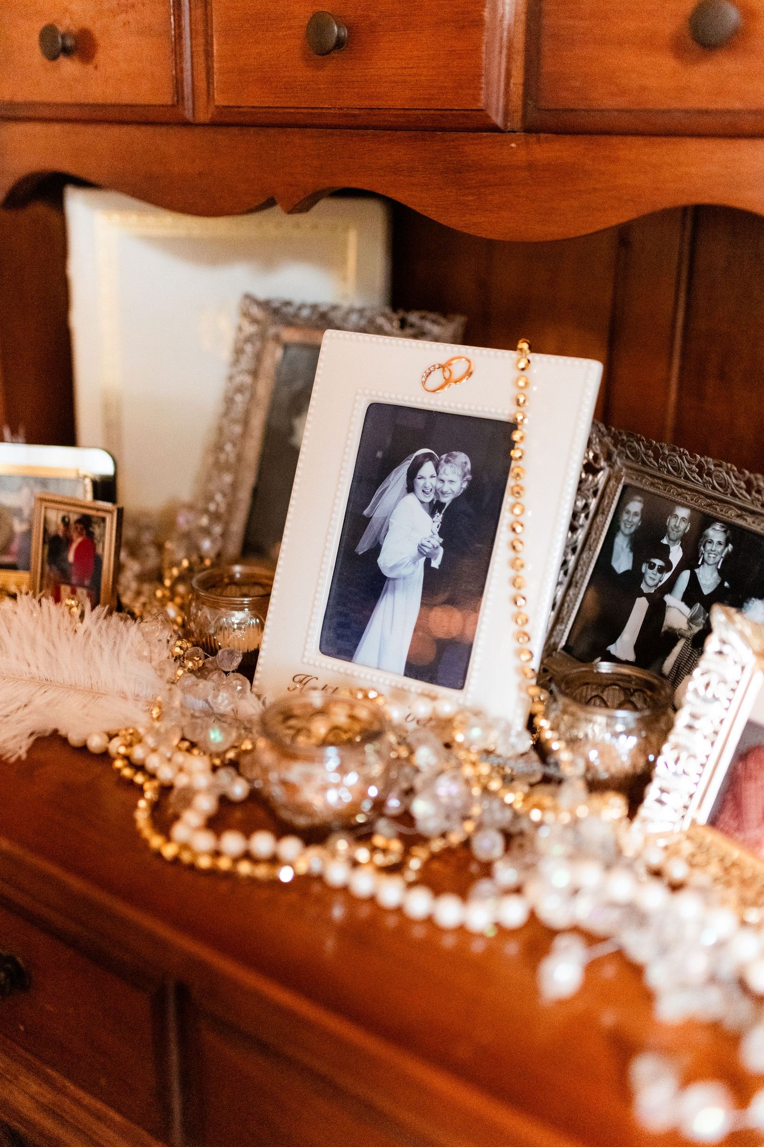 Vintage photographs displayed on wooden dresser with pearl necklace decorations and ornate frames.