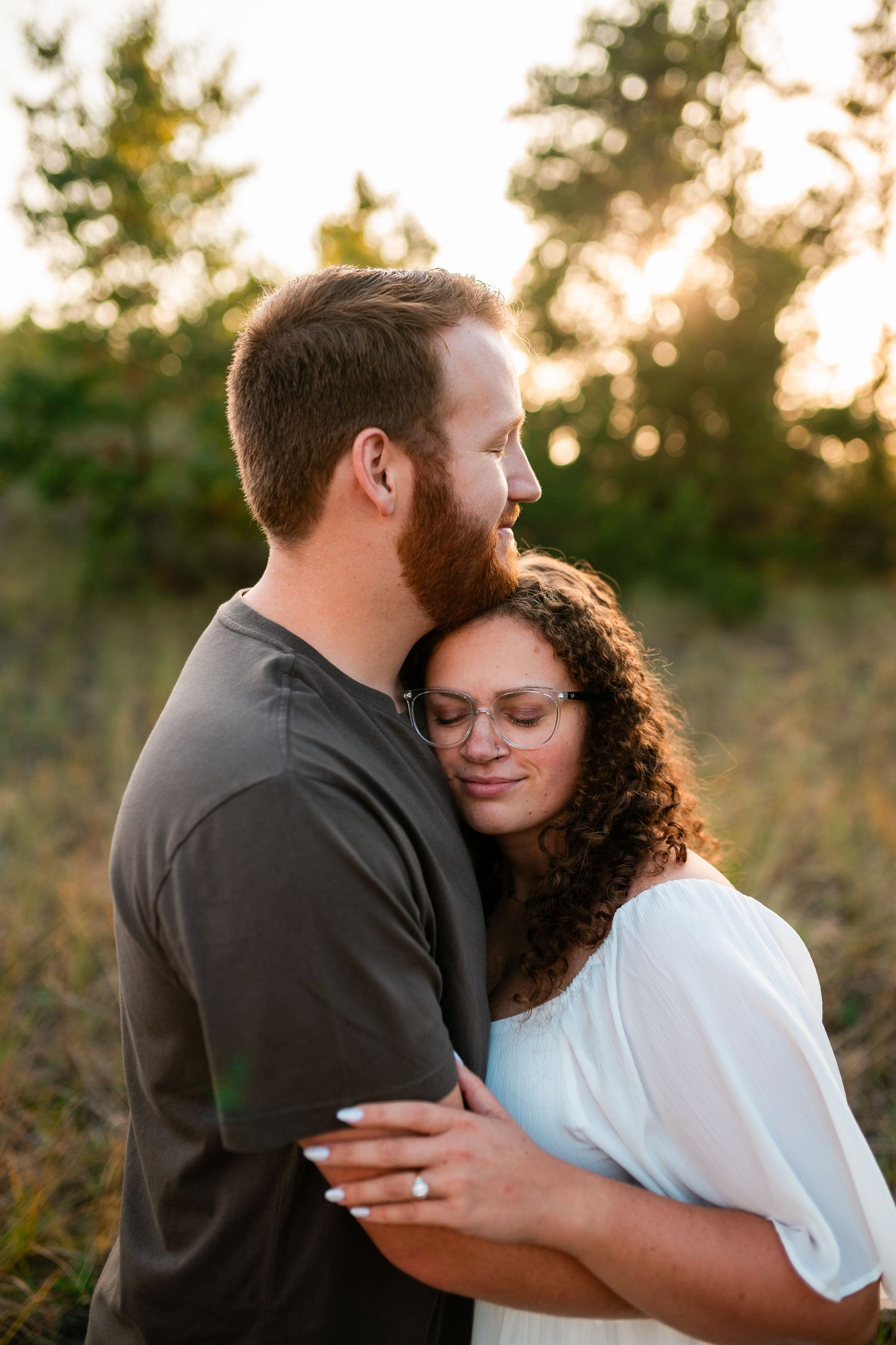 Couple embraces in golden sunset light among trees while sharing intimate moment in nature.