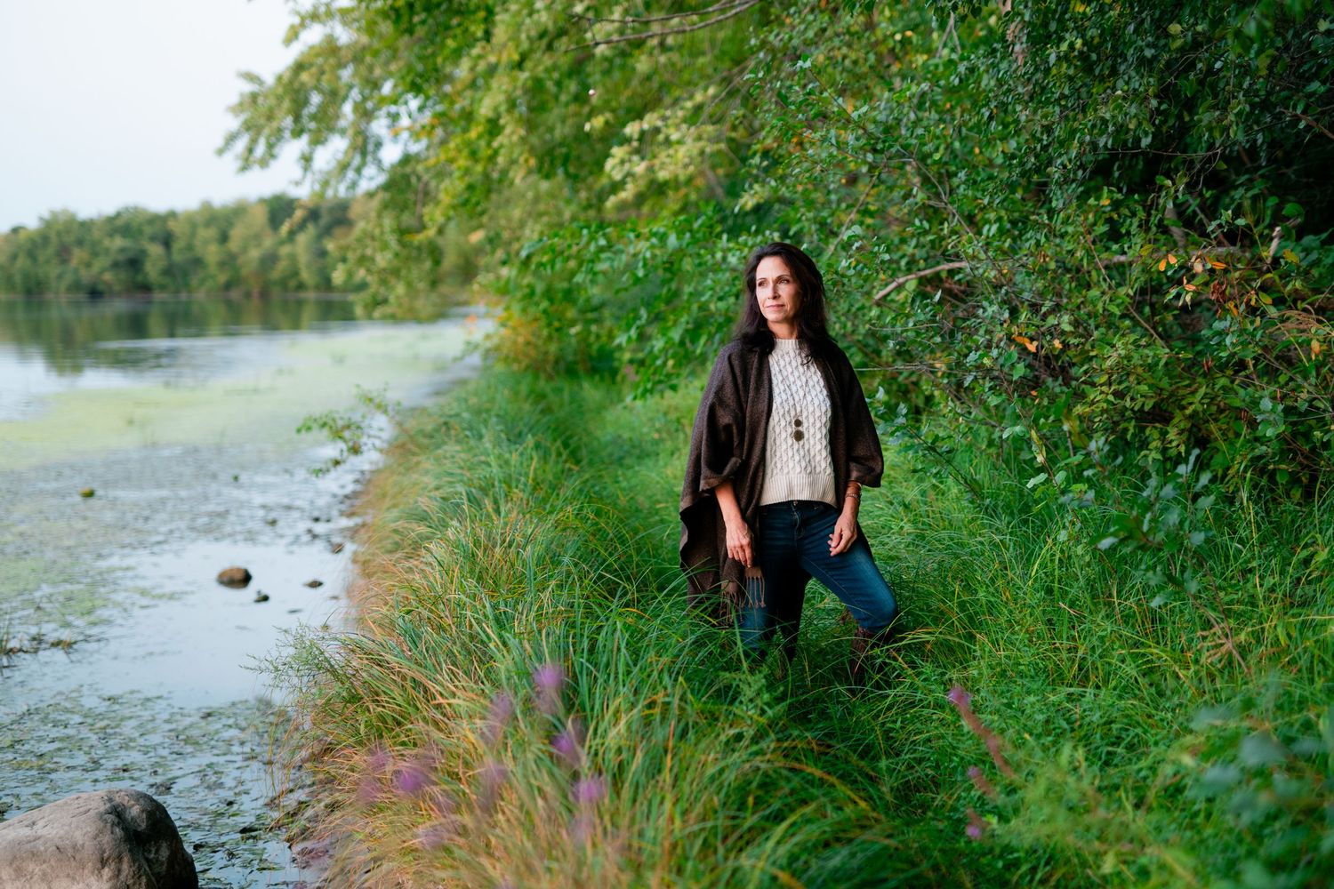 A scenic path along a lush riverbank with vibrant green foliage and calm waters in the background.