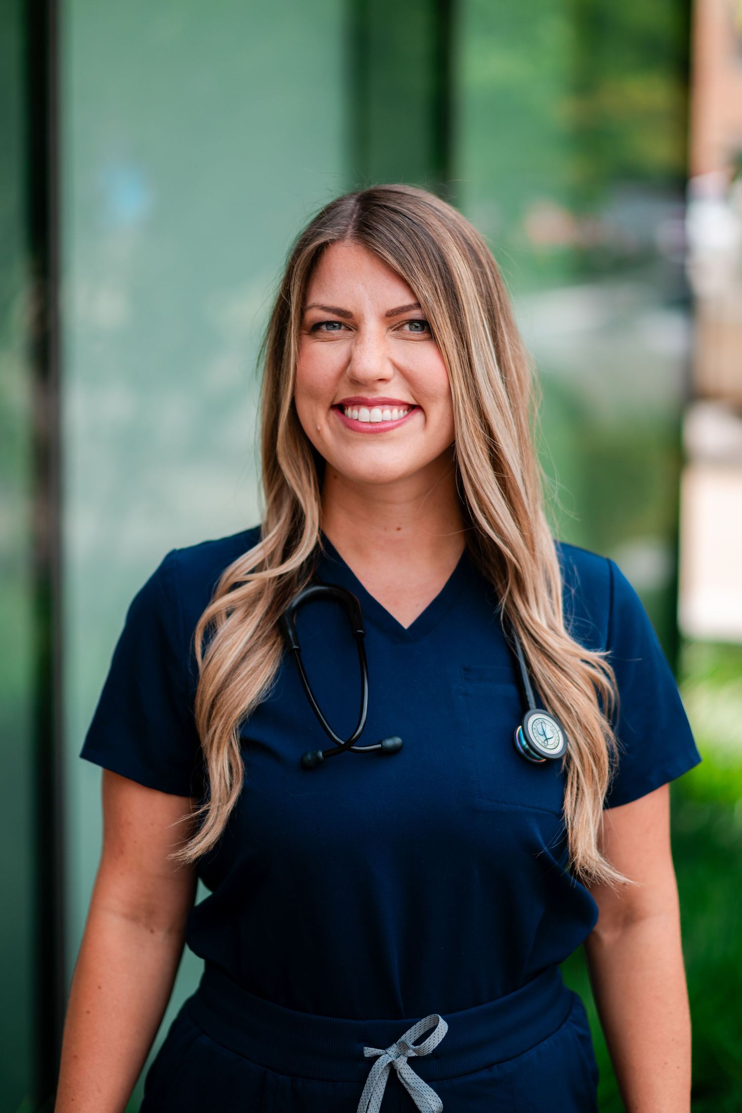 Healthcare professional in navy blue scrubs smiling warmly in a medical office setting.