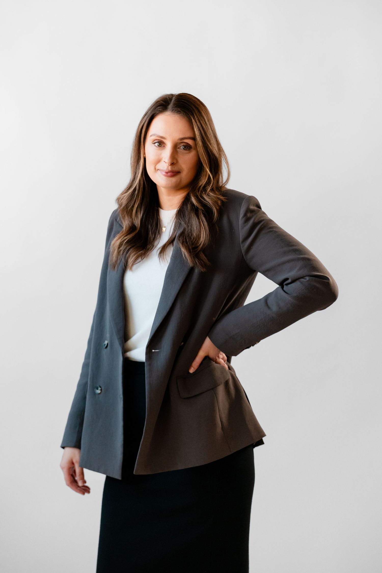 Professional lawyer wearing a black blazer and white top poses confidently against a light background in a photography studio setting.