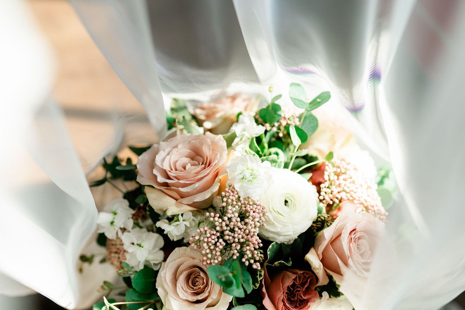 Elegant bridal bouquet with blush roses, white ranunculus, and greenery wrapped in soft gray ribbon.