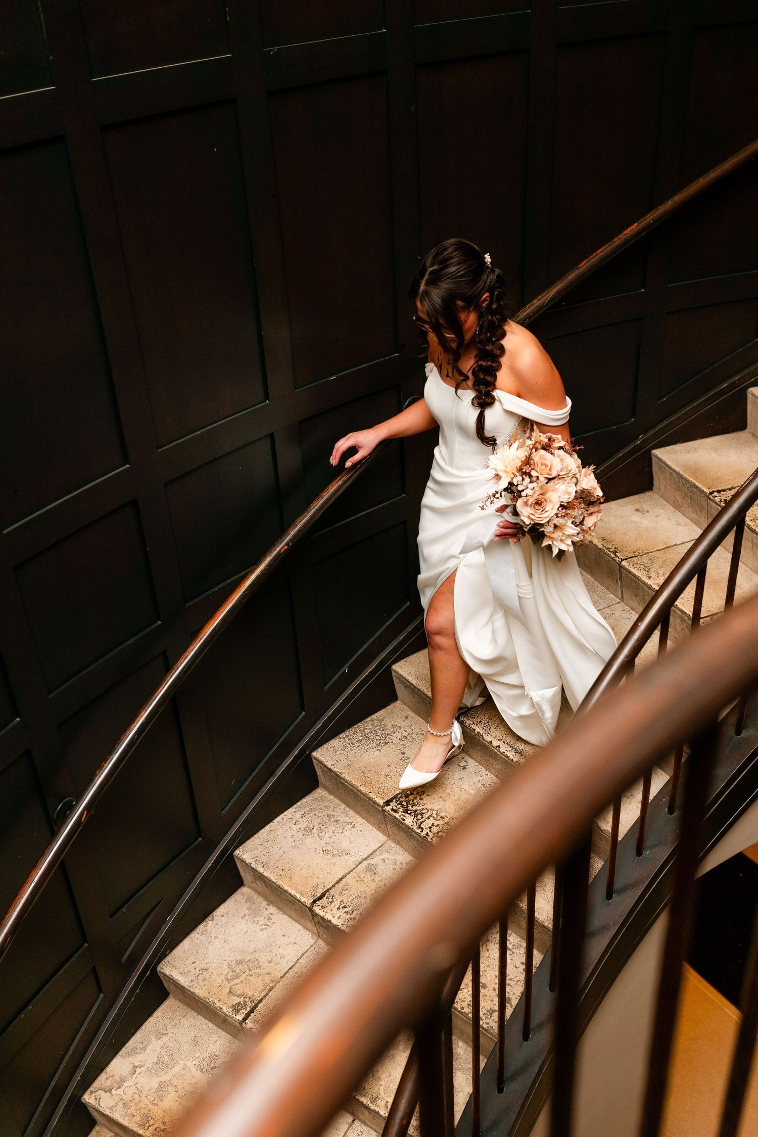 A person in a white dress sits on a spiral staircase with a dark railing, creating an elegant composition.