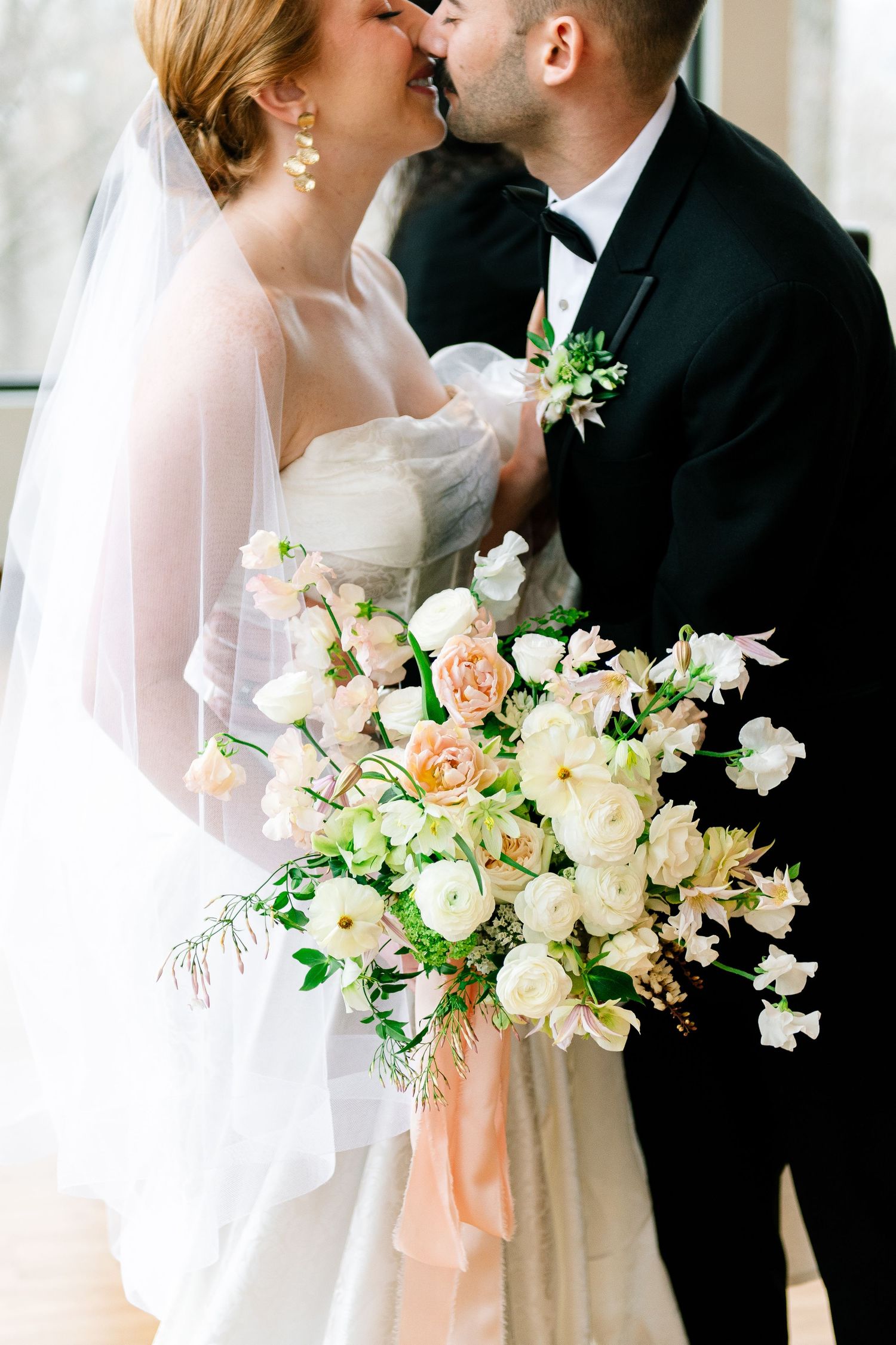 Romantic wedding couple shares an intimate moment with elegant peach and white floral bouquet.
