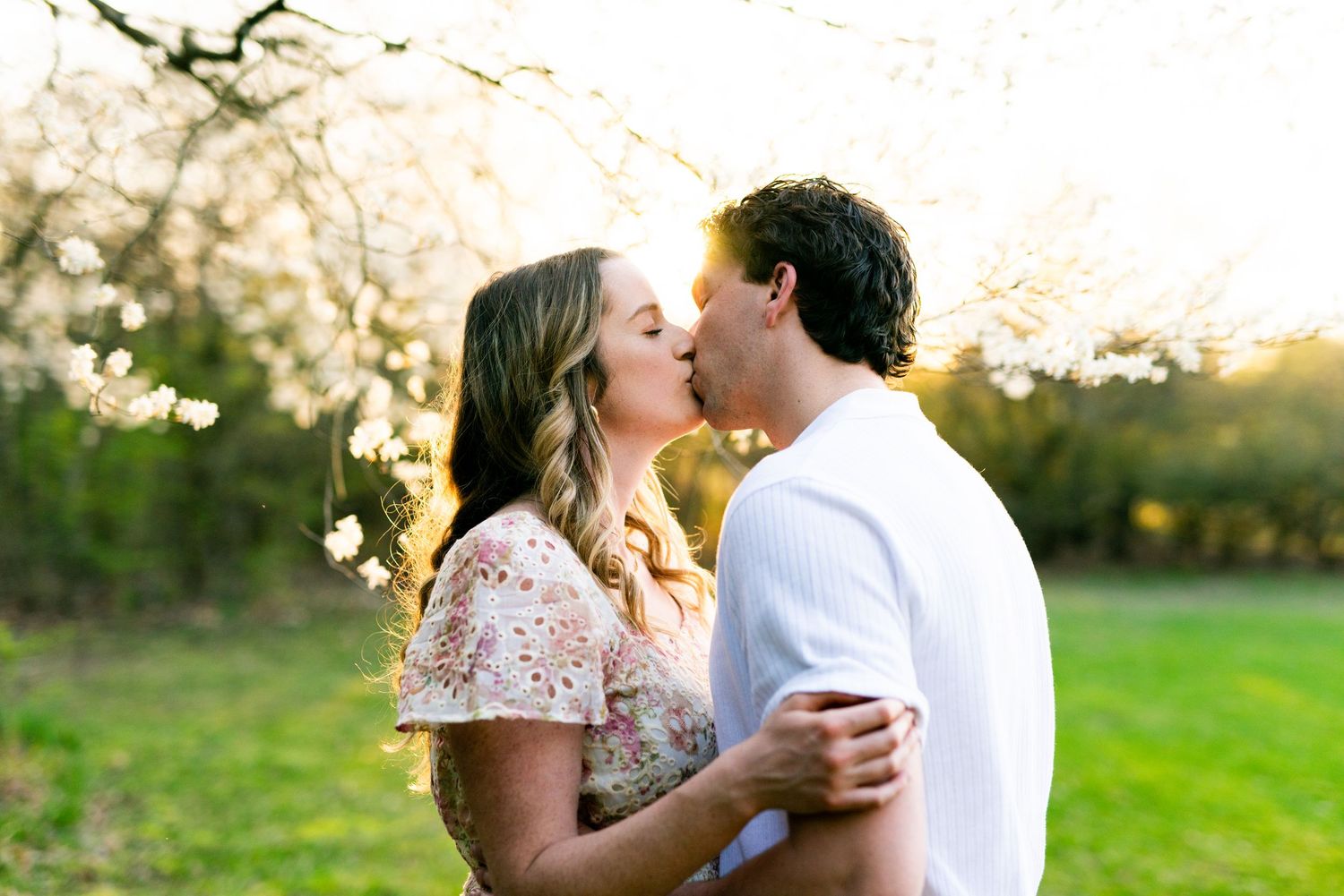 A romantic spring photo session in a blooming orchard at golden hour with soft sunlight filtering through the trees.