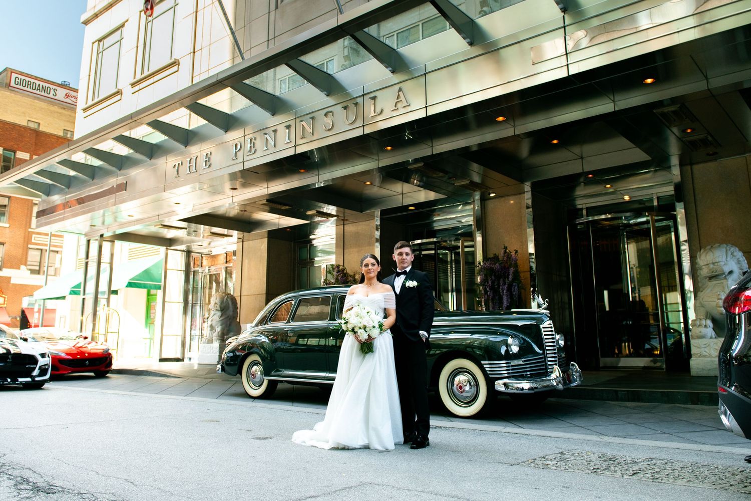 Bride and groom posing in front of The Peninsula Hotel with a vintage black car on their wedding day.