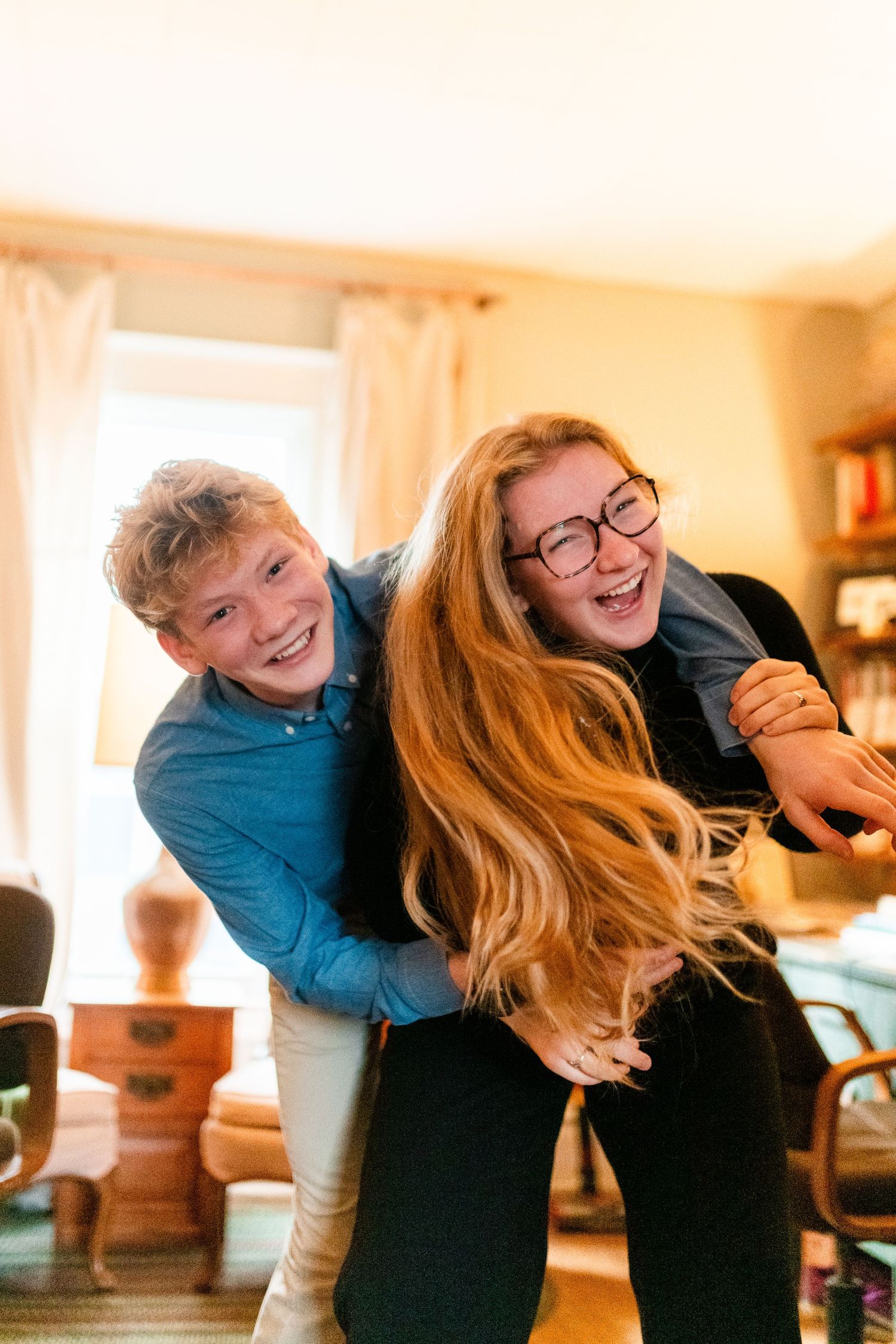 Two people share a joyful moment together while laughing and embracing in a warmly lit room.