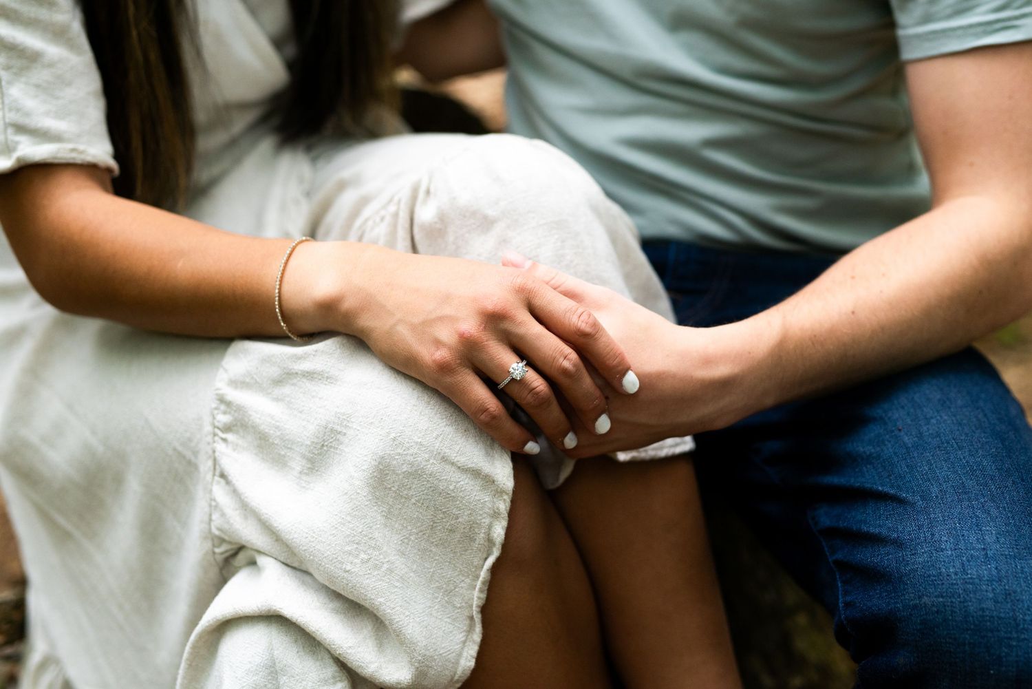 Close up photo showing hands gently touching and clasped together on laps while wearing casual attire.