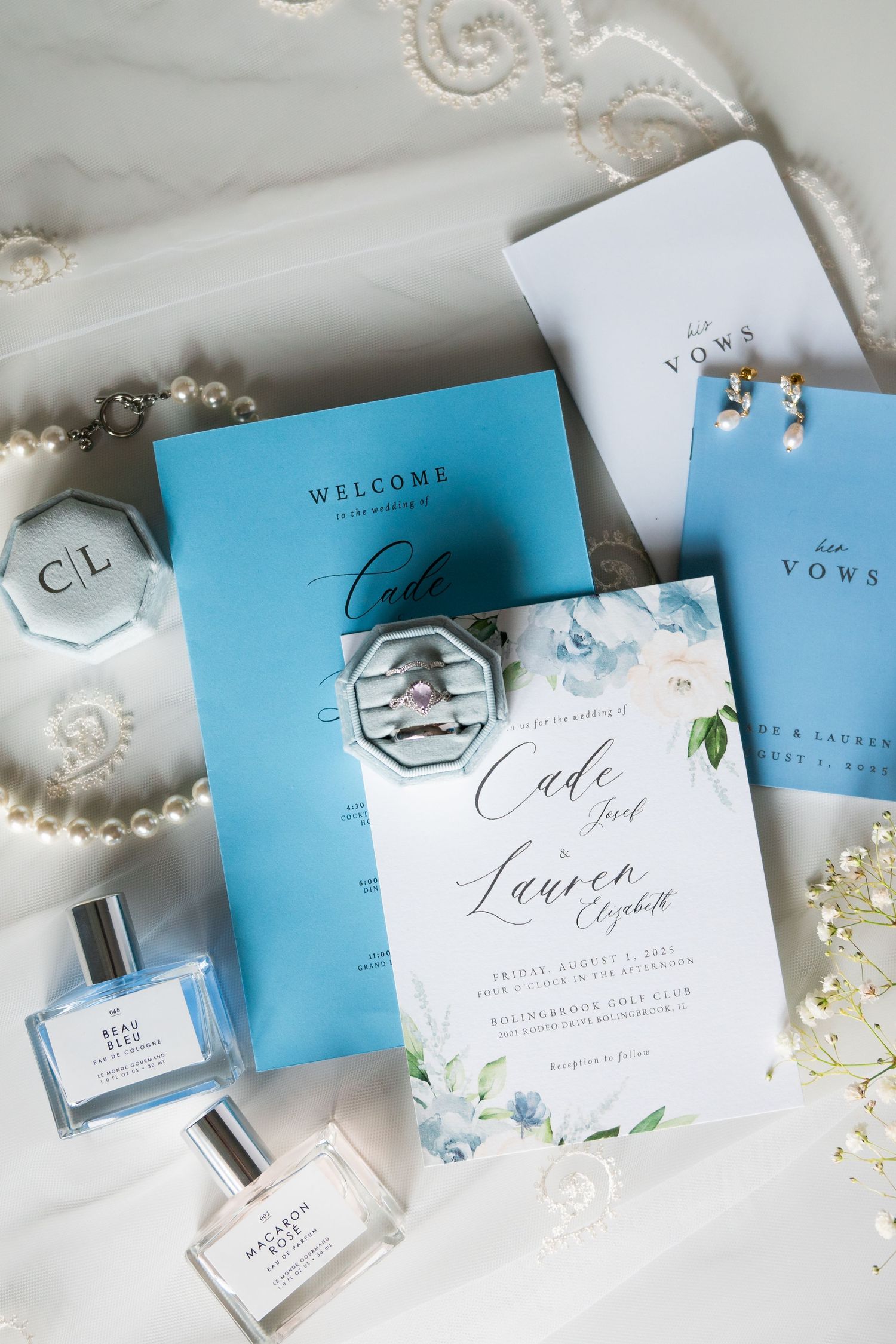 Elegant wedding stationery suite in light blue and white with pearl accents laid out on a white surface.