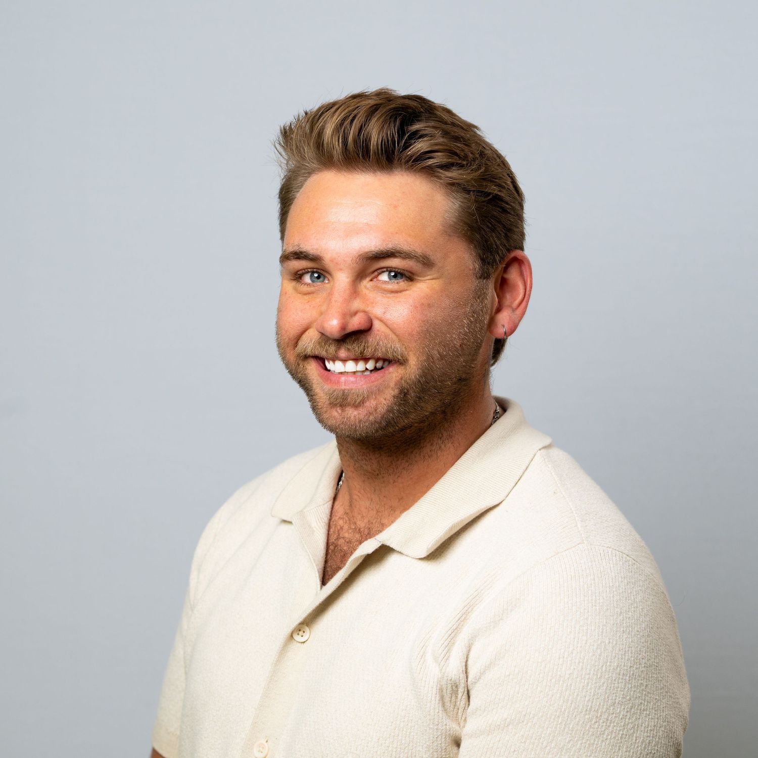 Smiling man with brown hair wearing a cream polo shirt against a light gray background for a grand rapids team headshot session