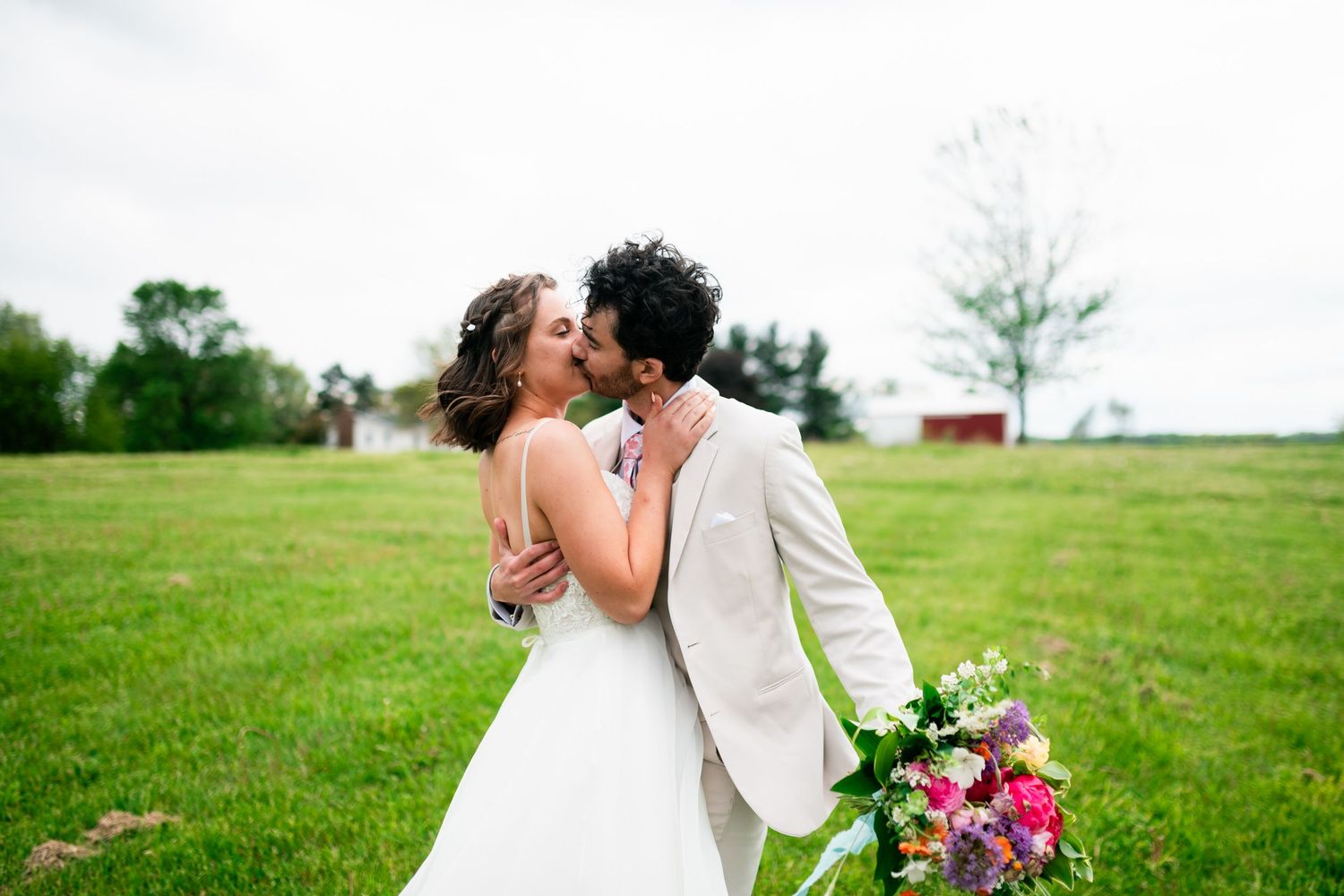 A romantic wedding couple shares a kiss in a lush green field during portraits at a timless grand rapids wedding