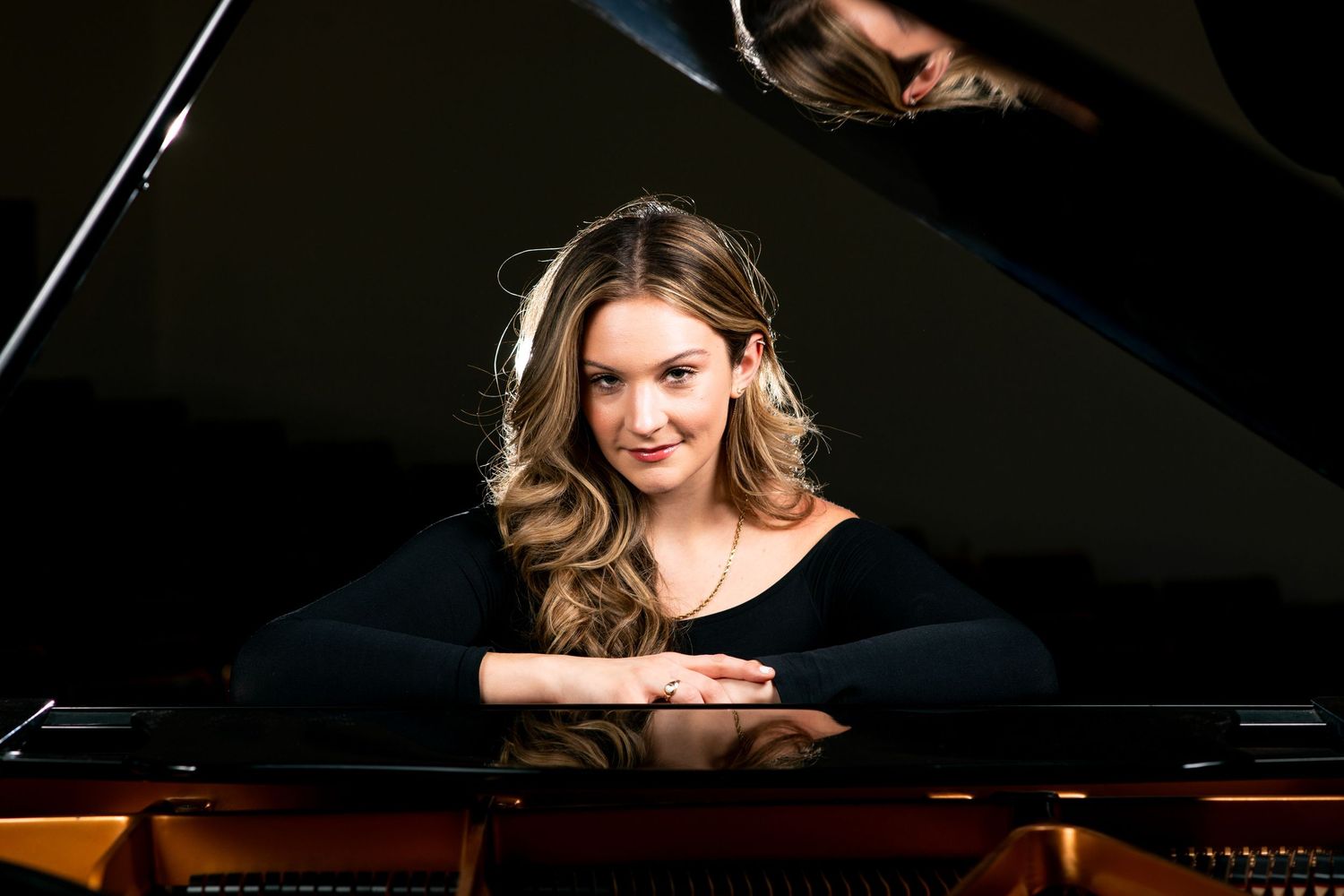 Professional musician plays grand piano in dramatic lighting during classical performance at concert hall.