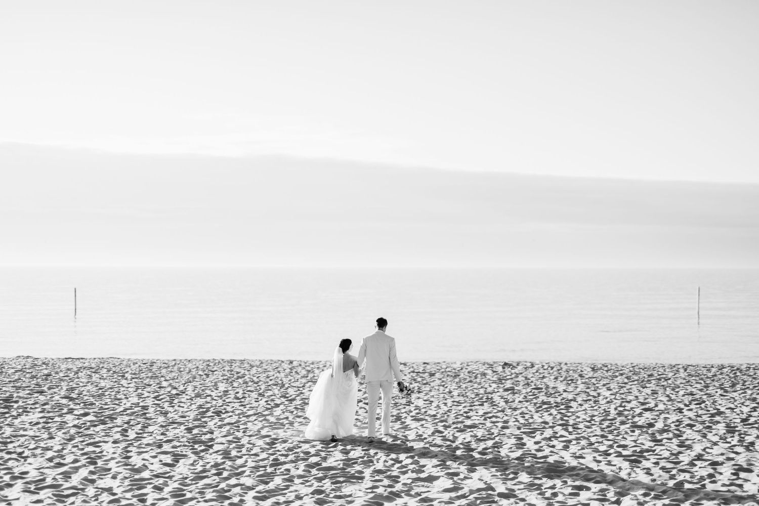 Two silhouetted figures stand on a vast white salt flat landscape under a cloudy sky.