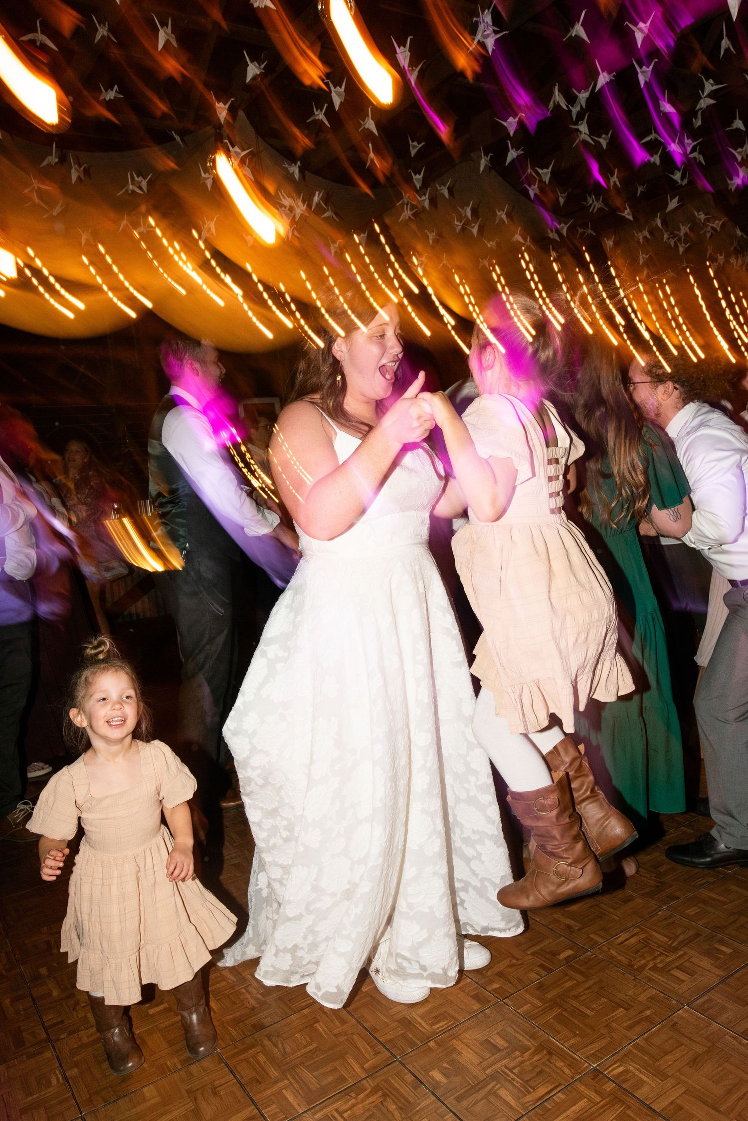 Wedding reception dance party with string lights overhead and people dancing on a wooden parquet floor.