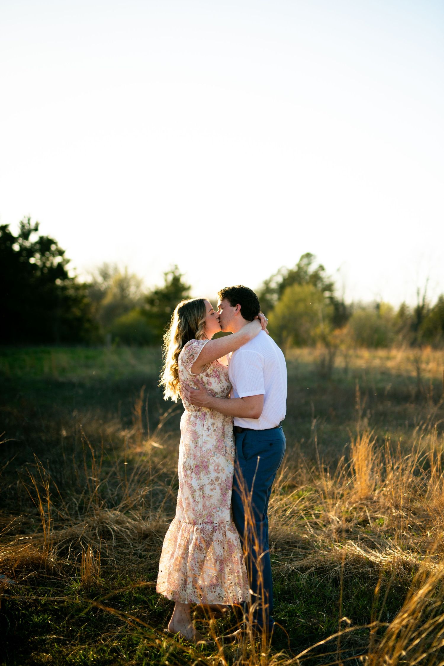 A couple embraces tenderly in a sun-drenched field of tall grass during golden hour.