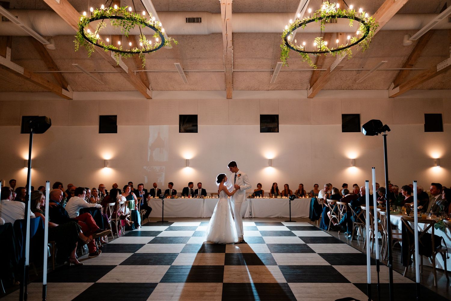 Grand rapids wedding reception with a black and white checkered floor and circular chandeliers overhead.