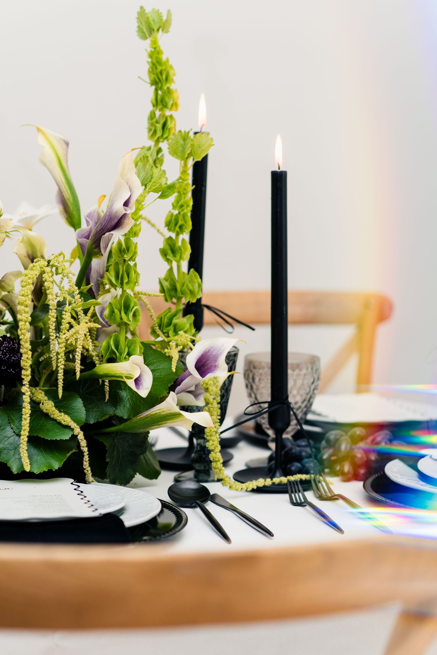 Elegant table setting with black candles, floral centerpiece, and iridescent CDs on a white tablecloth.
