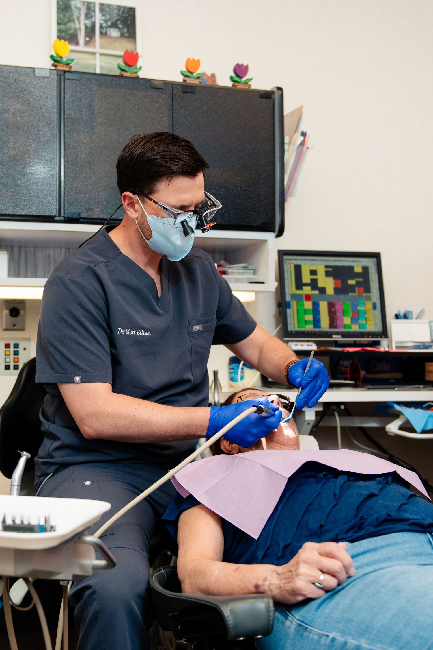 Dental professional in blue scrubs and face mask performs treatment on patient in modern medical office.
