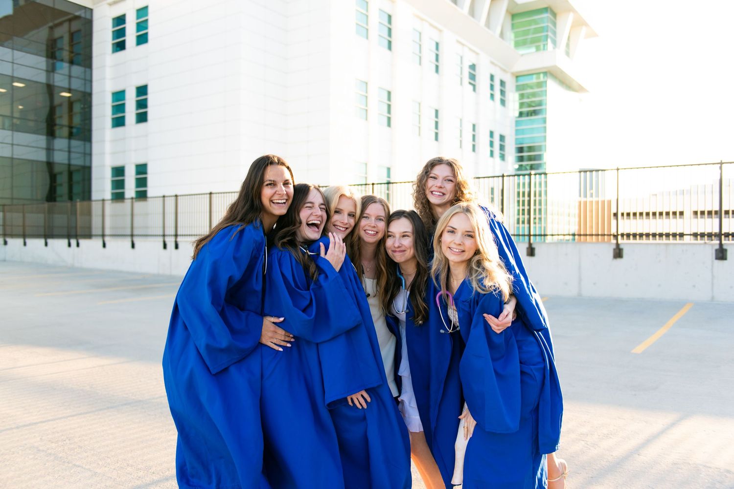 A group of students in bright blue graduation gowns laugh and smile while walking outside a building.