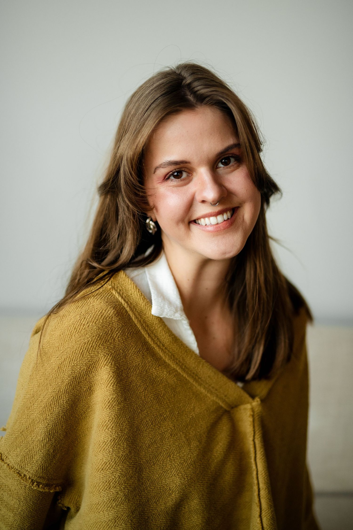 expressive portrait showing joyful emotions while wearing a mustard yellow sweater against a light background.