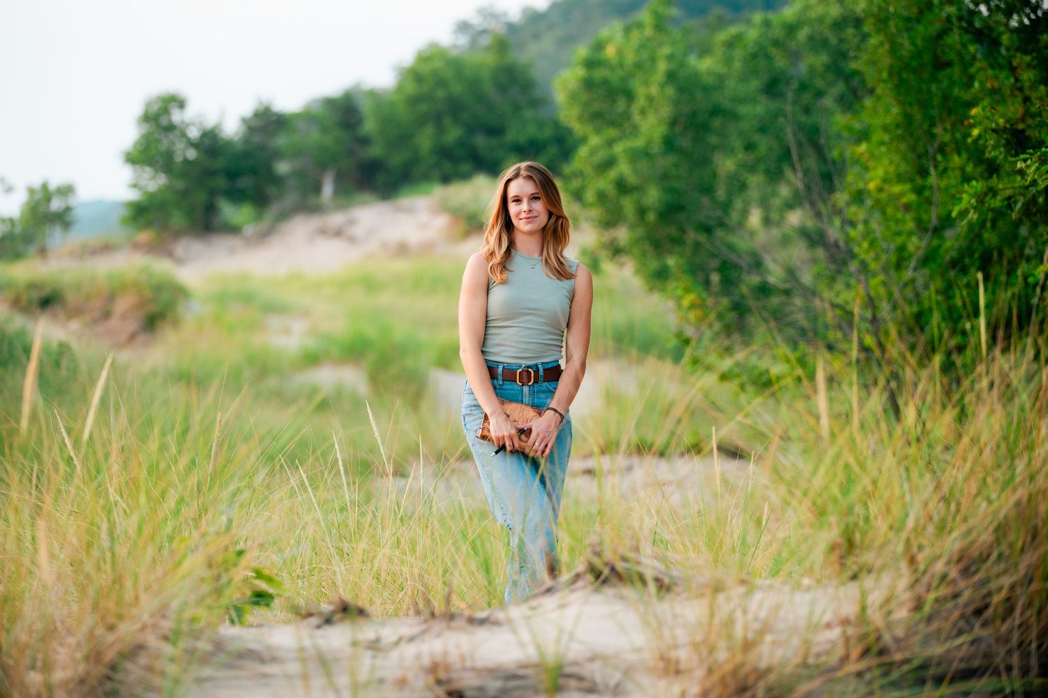 Woman in blue dress walks through tall grass in a sunny field during golden hour photography session.