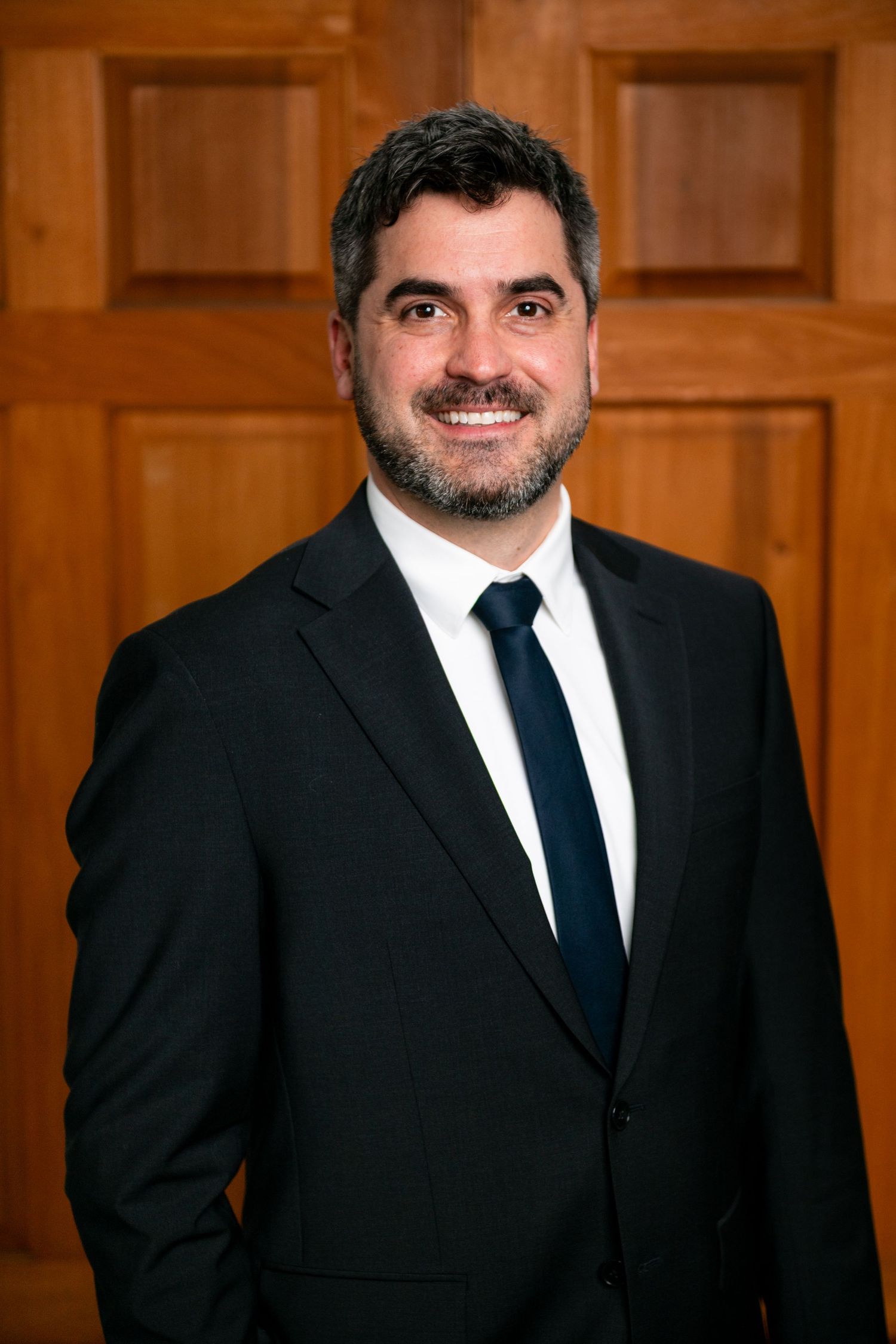 Grand Rapids Professional man in dark suit and navy tie smiling confidently in front of wooden door background.
