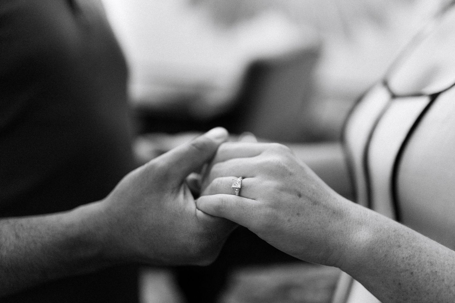 Black and white photo of a couple holding hands, showcasing a diamond engagement ring on the woman's finger.