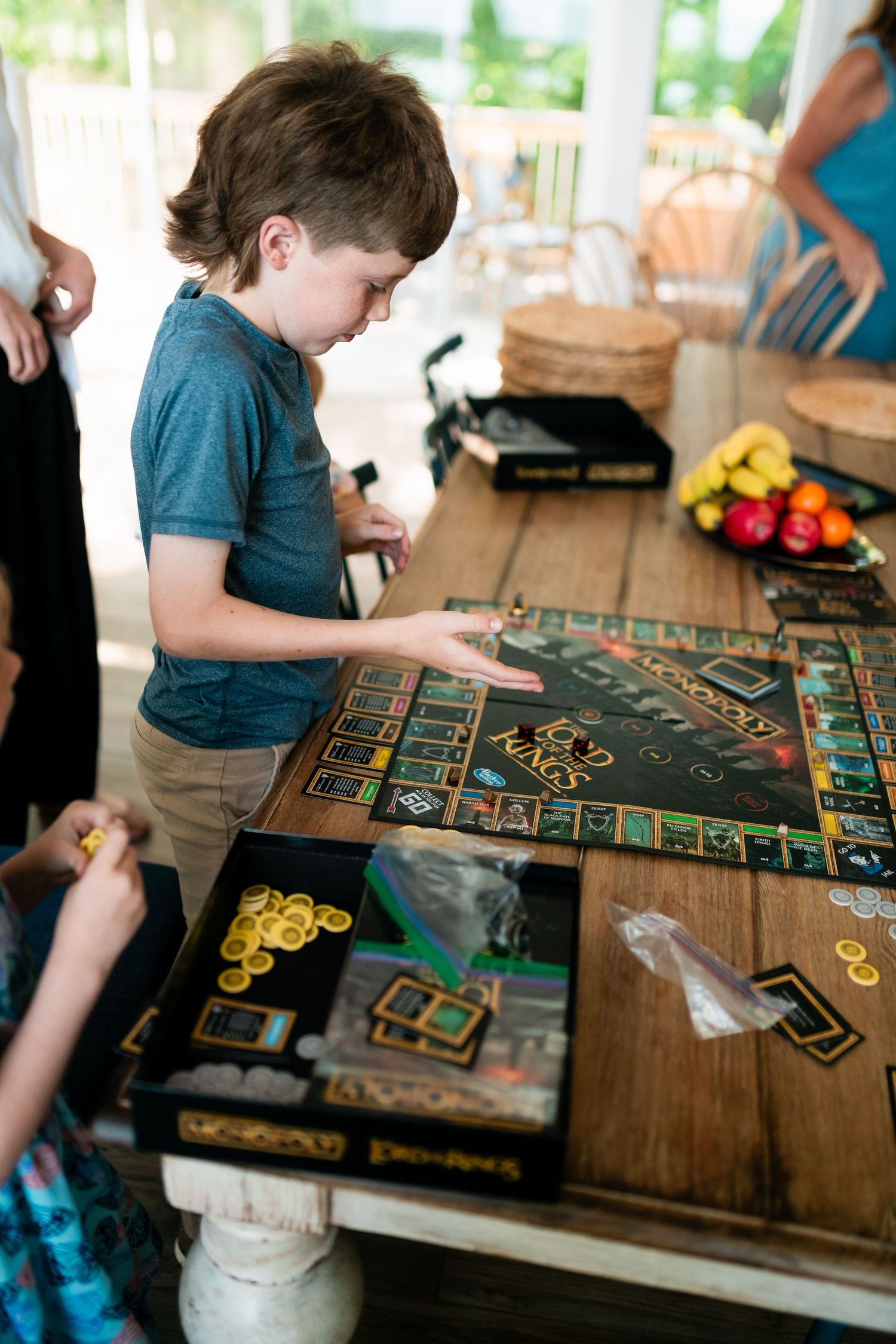 Person playing a board game with gold tokens and cards on a wooden table during a tabletop gaming session.