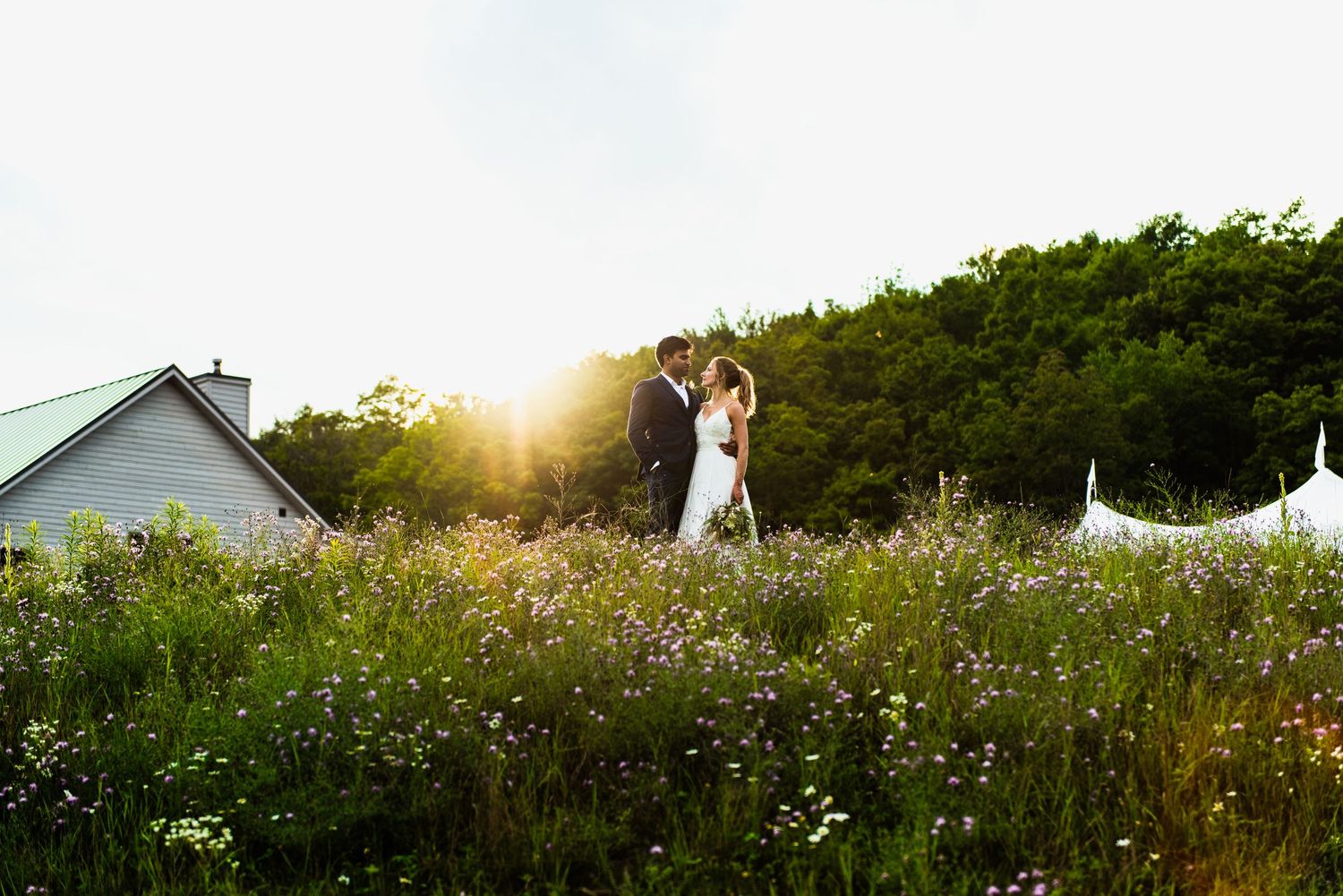Newlyweds pose together in a field of wildflowers during golden hour sunset for romantic wedding photos.