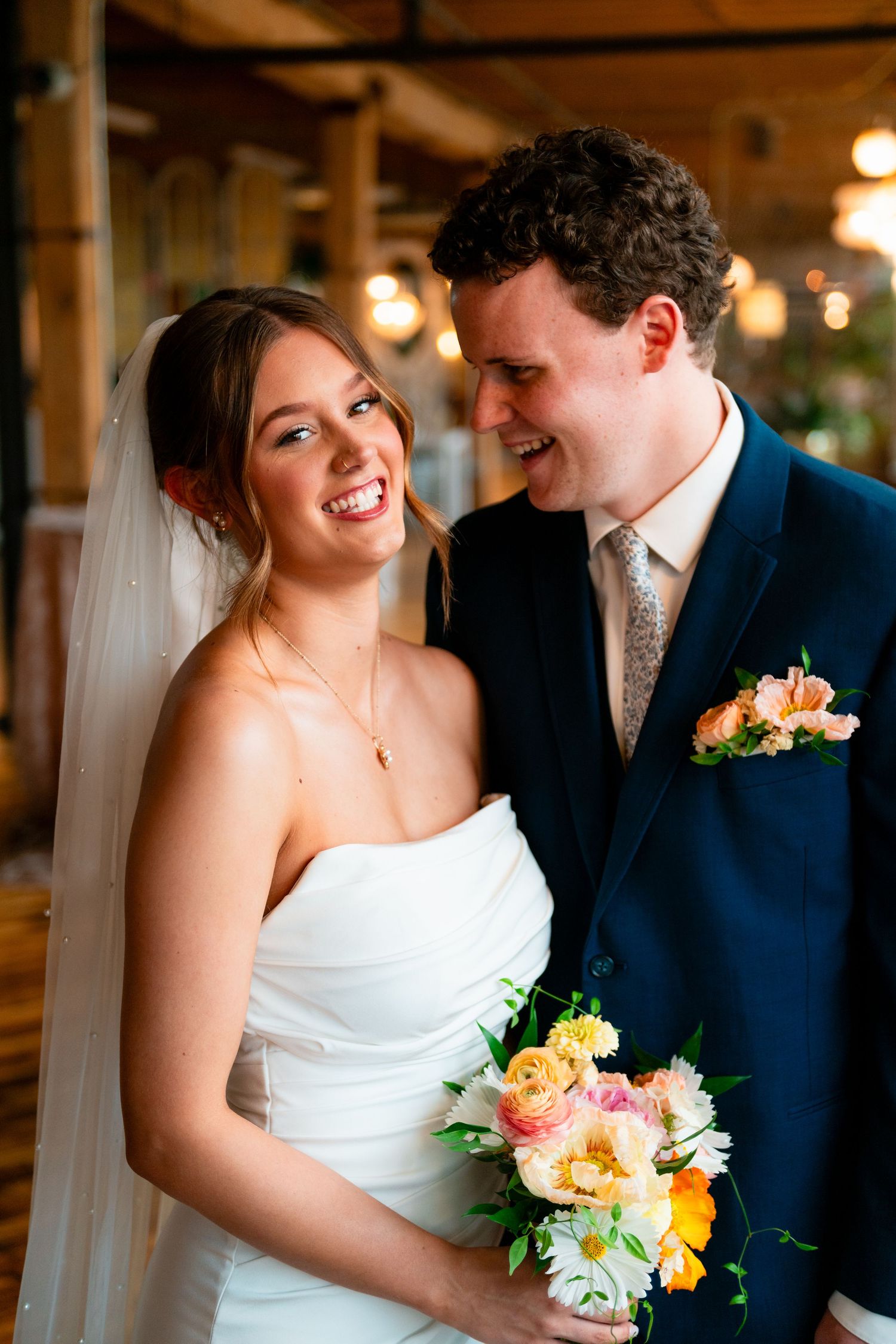A romantic wedding moment captured in warm indoor lighting with a colorful peach and yellow floral bouquet.