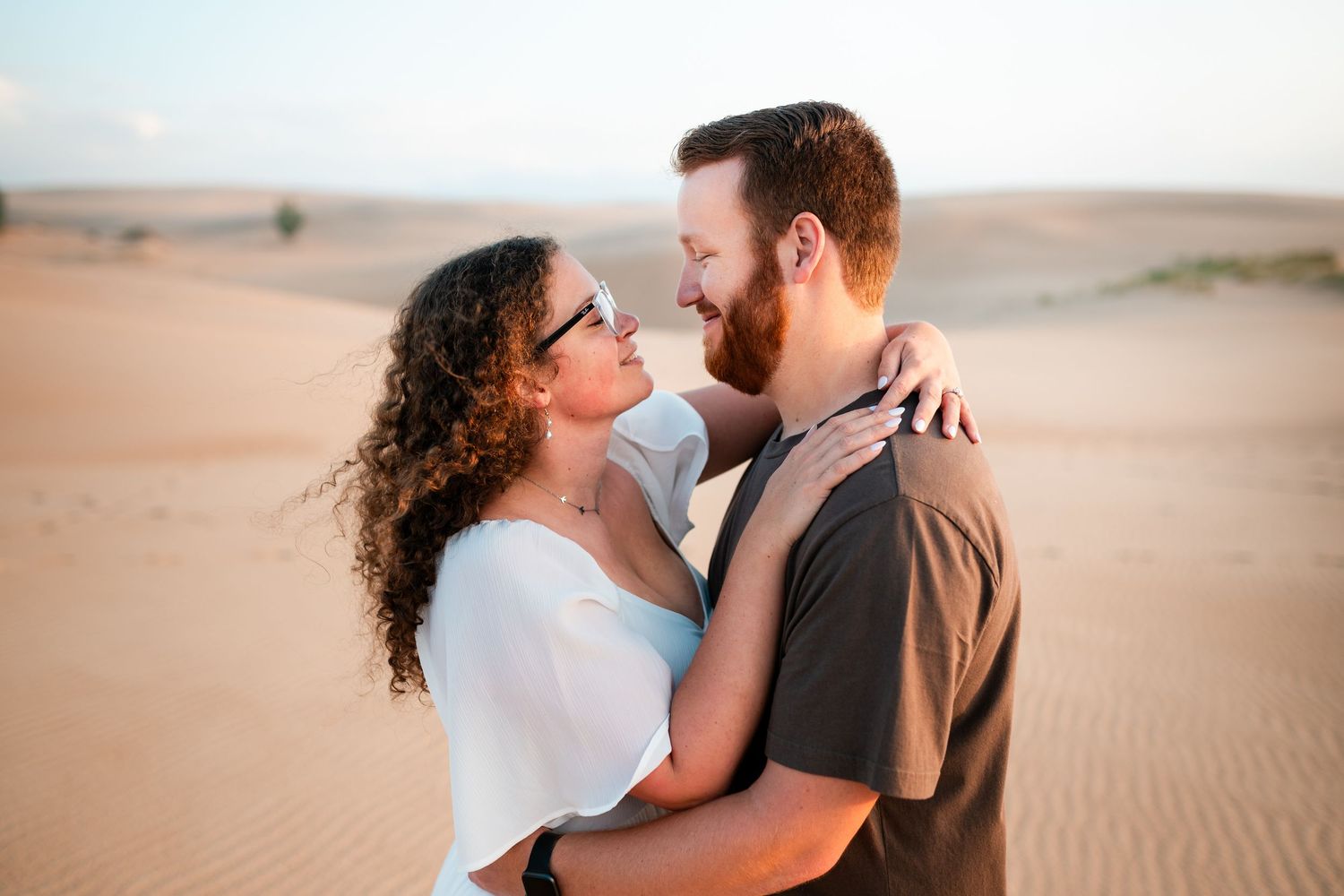 Couple embracing and gazing at each other romantically in a sandy desert landscape at golden hour.