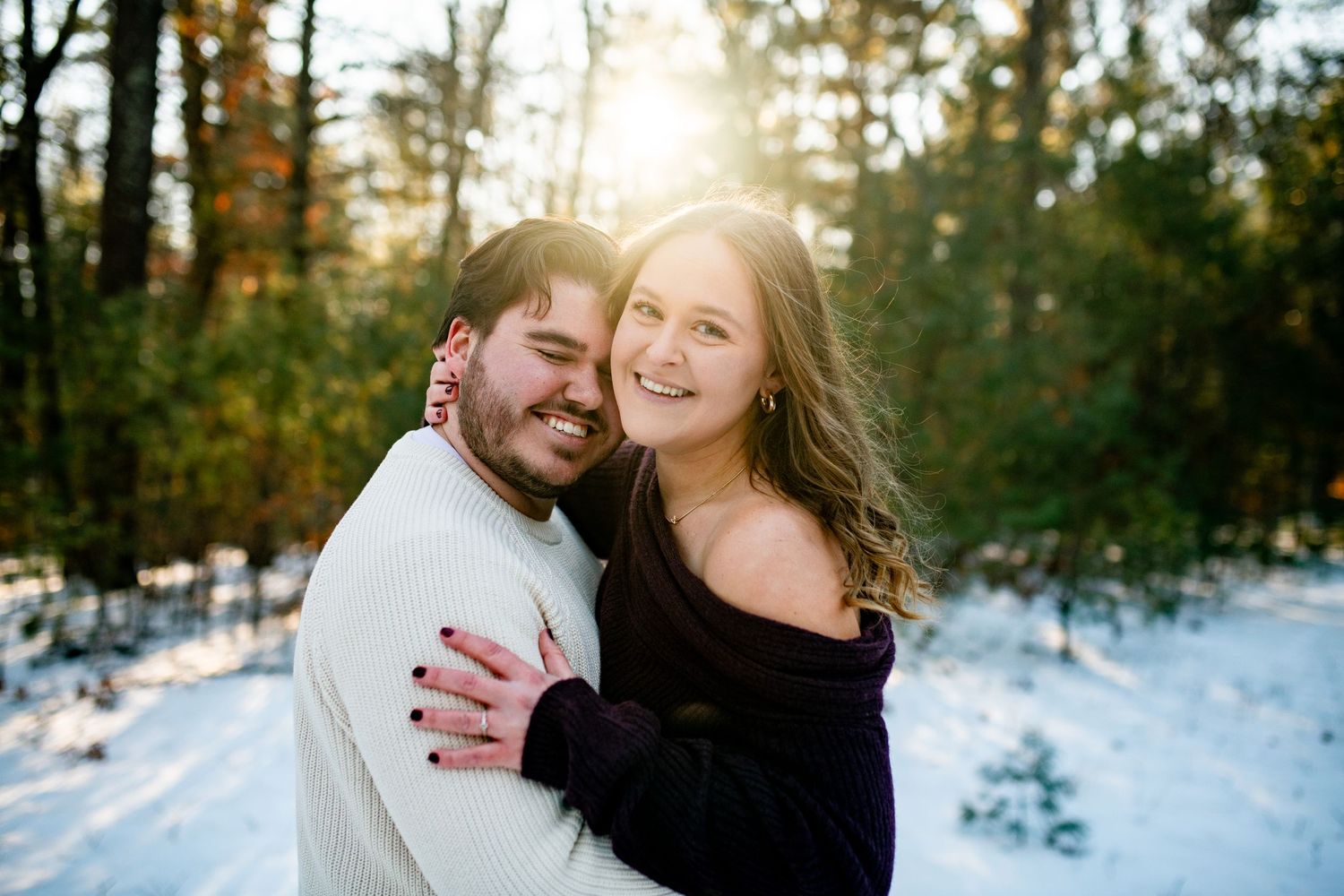 A couple shares a romantic moment in the snowy woods during a winter engagement photo session.