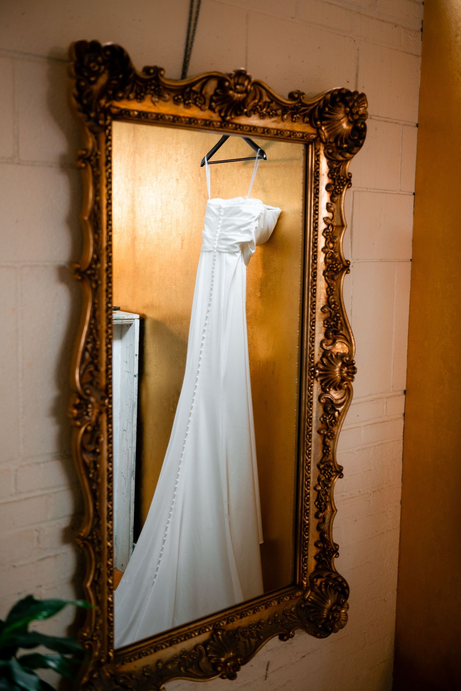 A white wedding dress hangs elegantly against ornate gold-framed mirrors on a white wall, creating a reflection sequence.