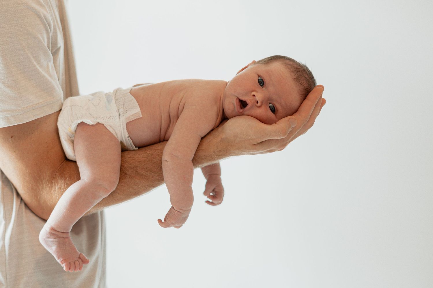 Sleeping newborn baby cradled in parent's arms against white background at lifestyle photoshoot in Augusta GA.