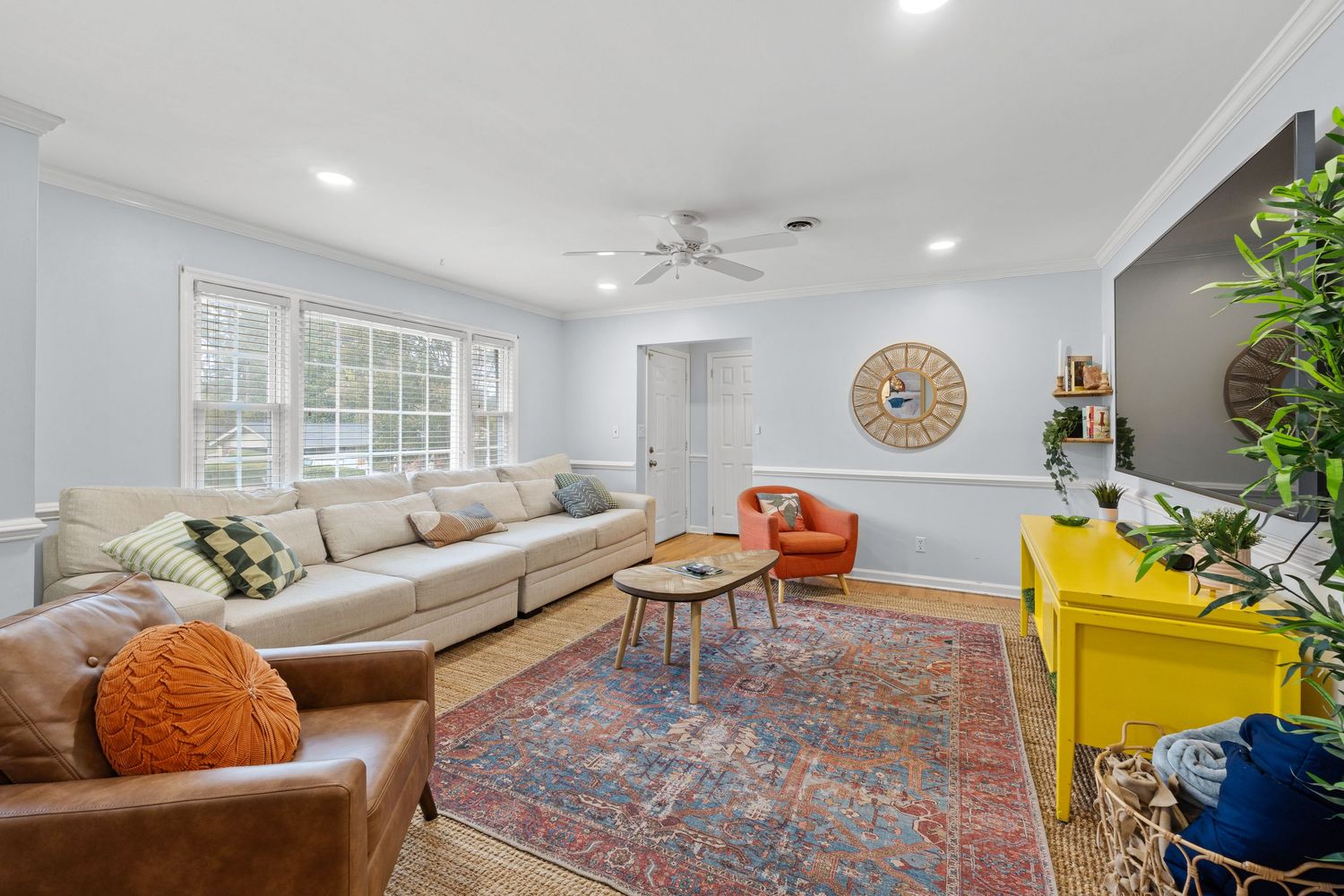Modern living room with beige sectional, brown leather chairs, colorful rug, yellow accent chair and decorative lighting.