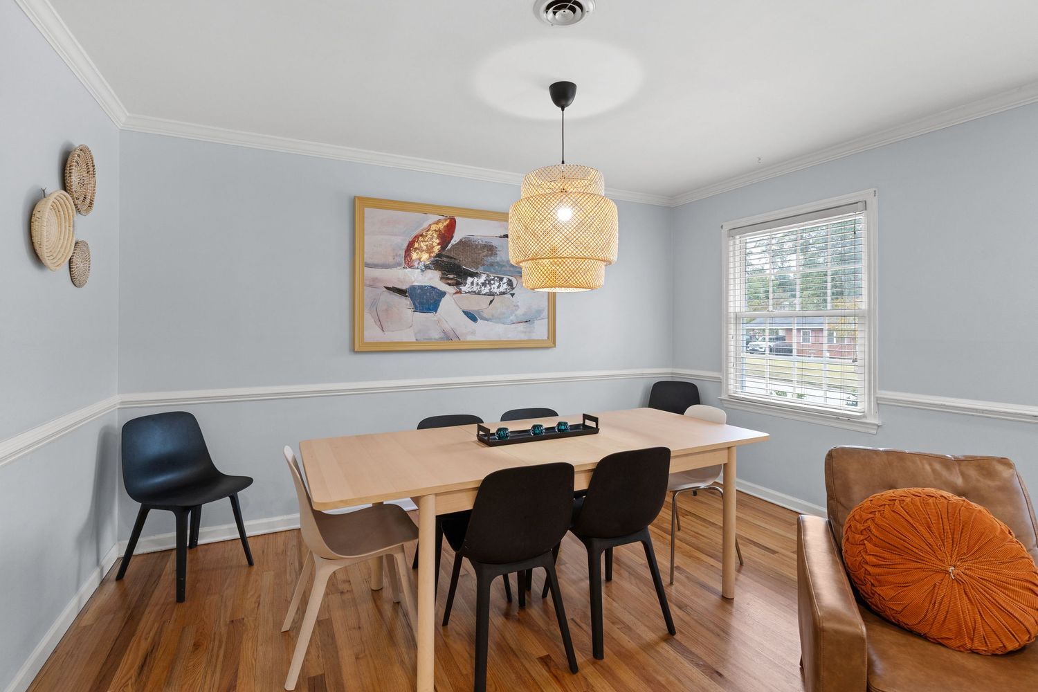 Contemporary dining area with black chairs, wooden table, and bright yellow accent chair against light walls.
