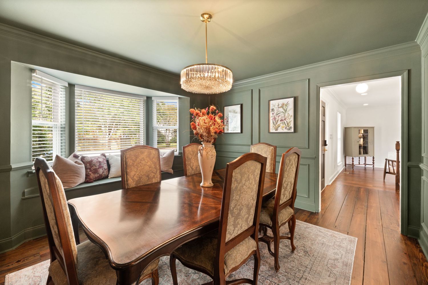 Elegant dining room with sage green walls, crystal chandelier and traditional wooden furniture for real estate photography in Augusta, GA.
