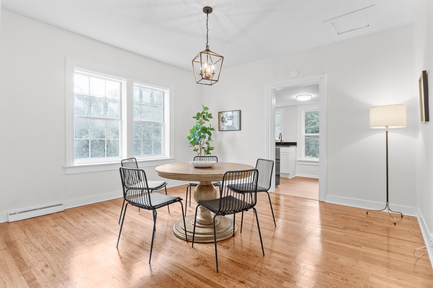 Bright dining area with pendant lighting, wooden table, and modern chairs on hardwood flooring.