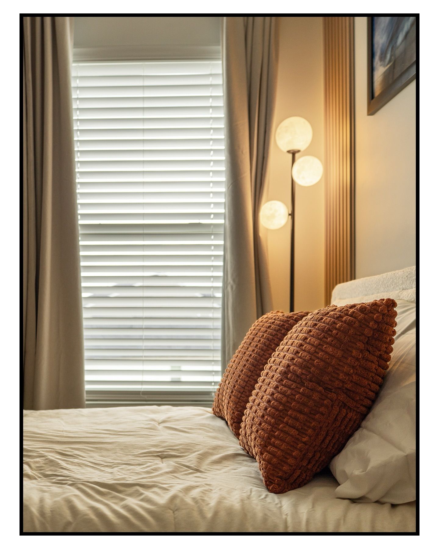 Serene bedroom with white bedding, rust-colored throw pillows, and modern wall sconce lighting for real estate photography in Augusta, GA.