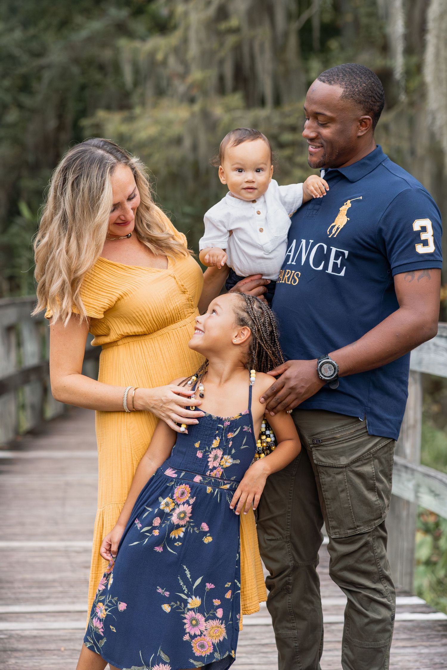 Family sharing joyful moments together on wooden boardwalk surrounded by trees for portrait photography in Augusta, GA.