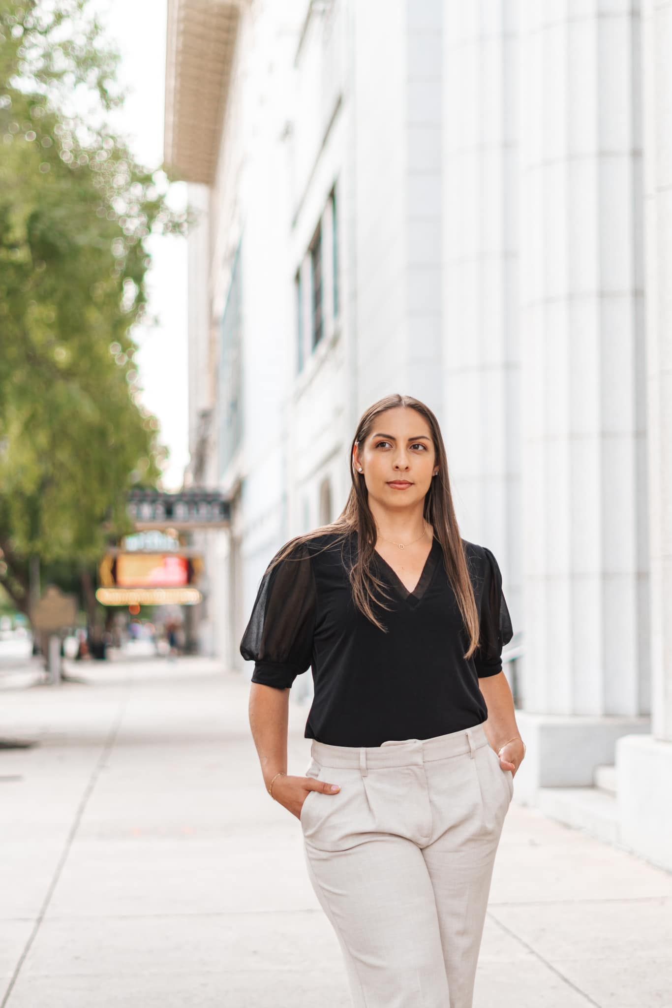 Business professional in black top and light pants poses near white columns in Augusta, GA.